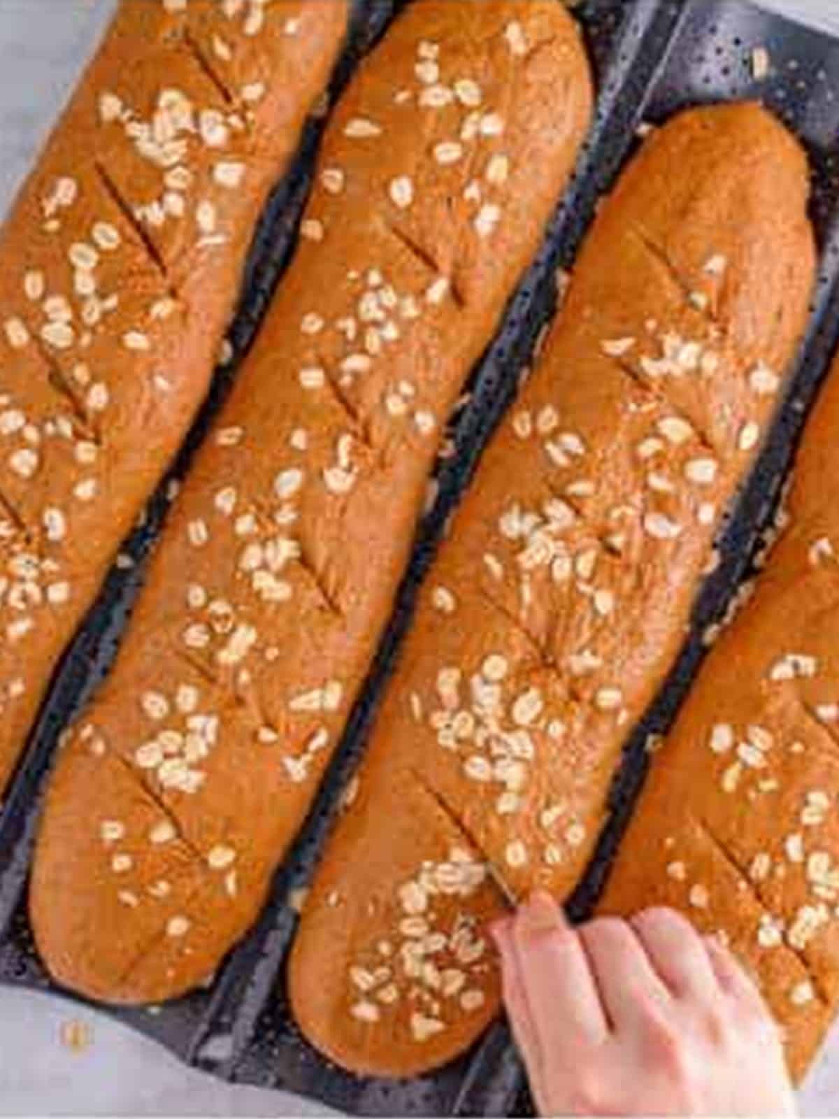 Brown bread baguettes scored across the tops before baking.