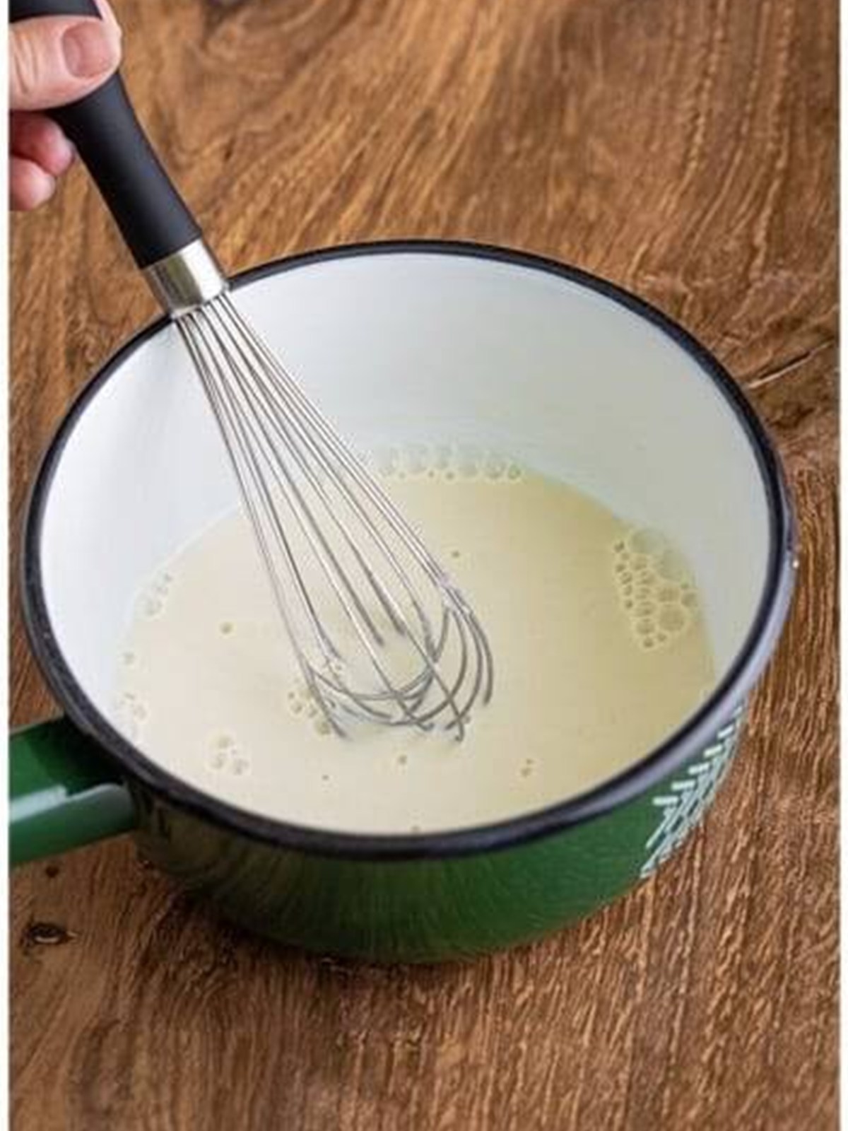 Whisking flour into milk in a saucepan for brown sugar frosting.