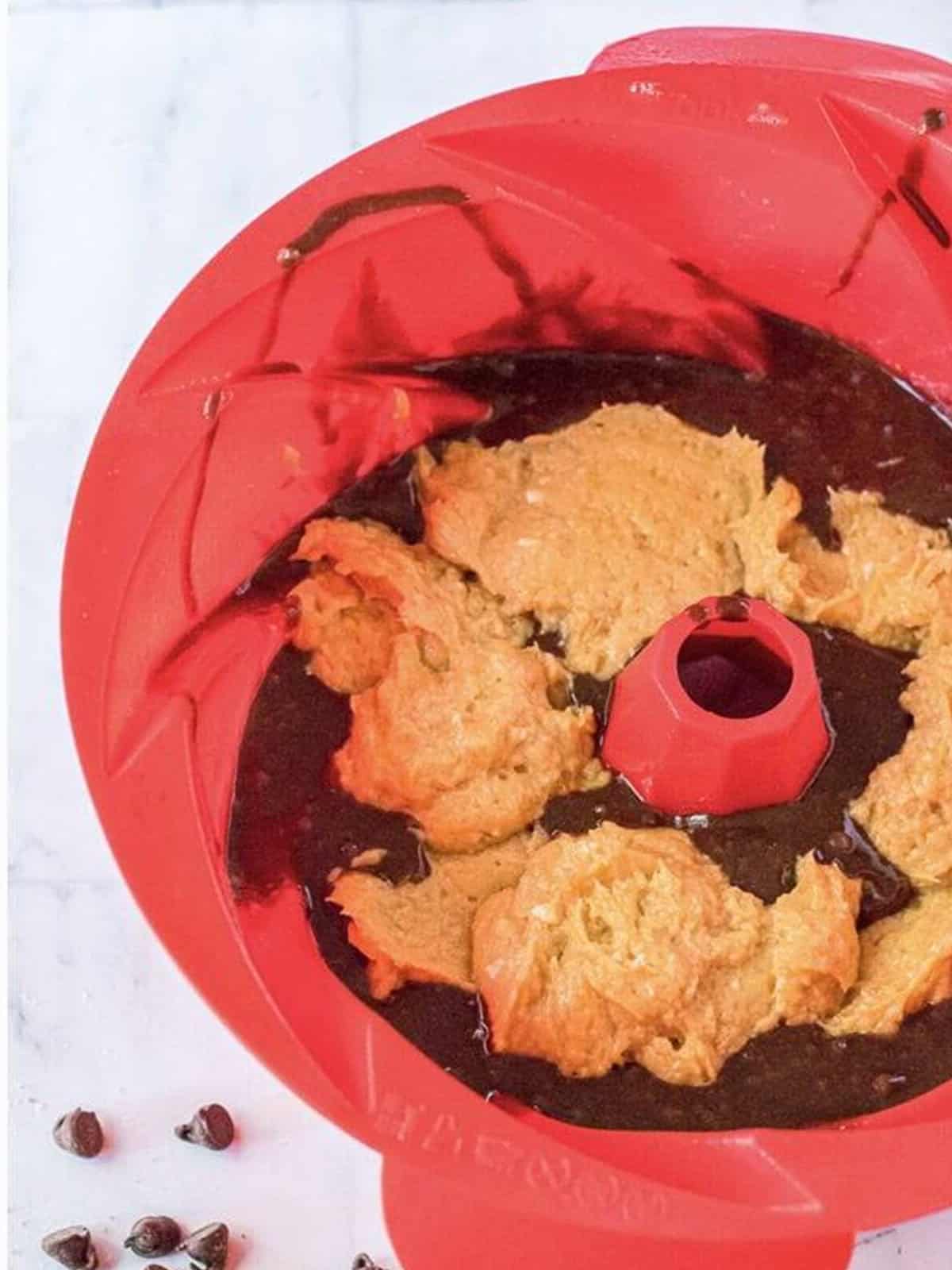 Brownie cake batter layered with dollops of peanut butter filling in a bundt pan.