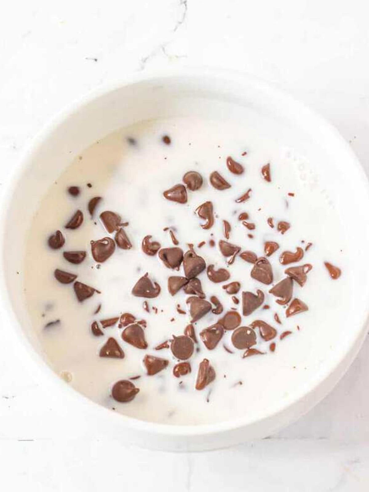 Chocolate chips and hot heavy cream in a bowl to make ganache for brownie cake.