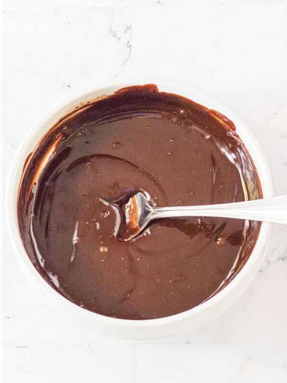 Smooth chocolate ganache stirred in a bowl to drizzle over brownie cake.
