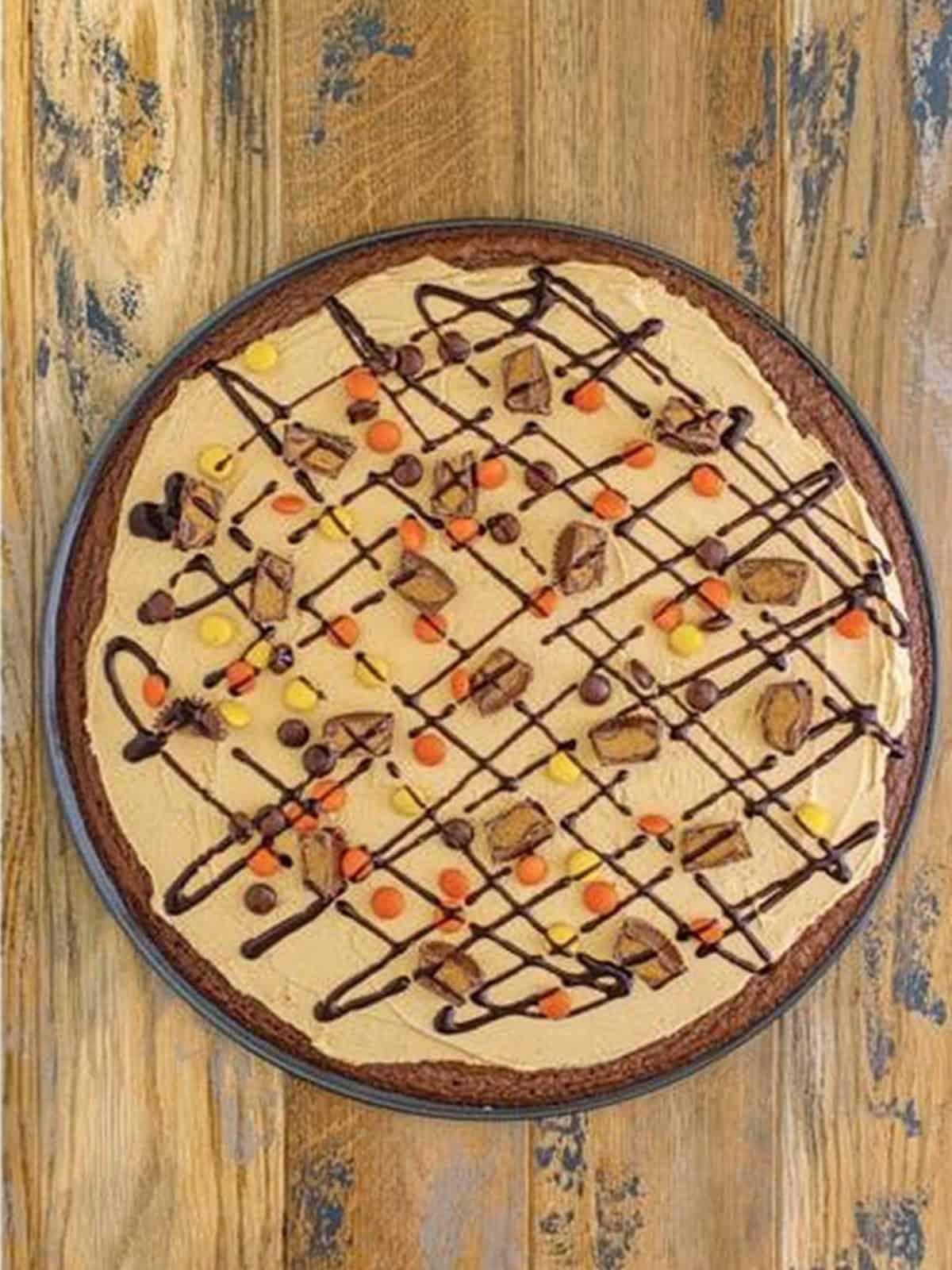 The finished brownie pizza drizzled with chocolate syrup and loaded with candy toppings.