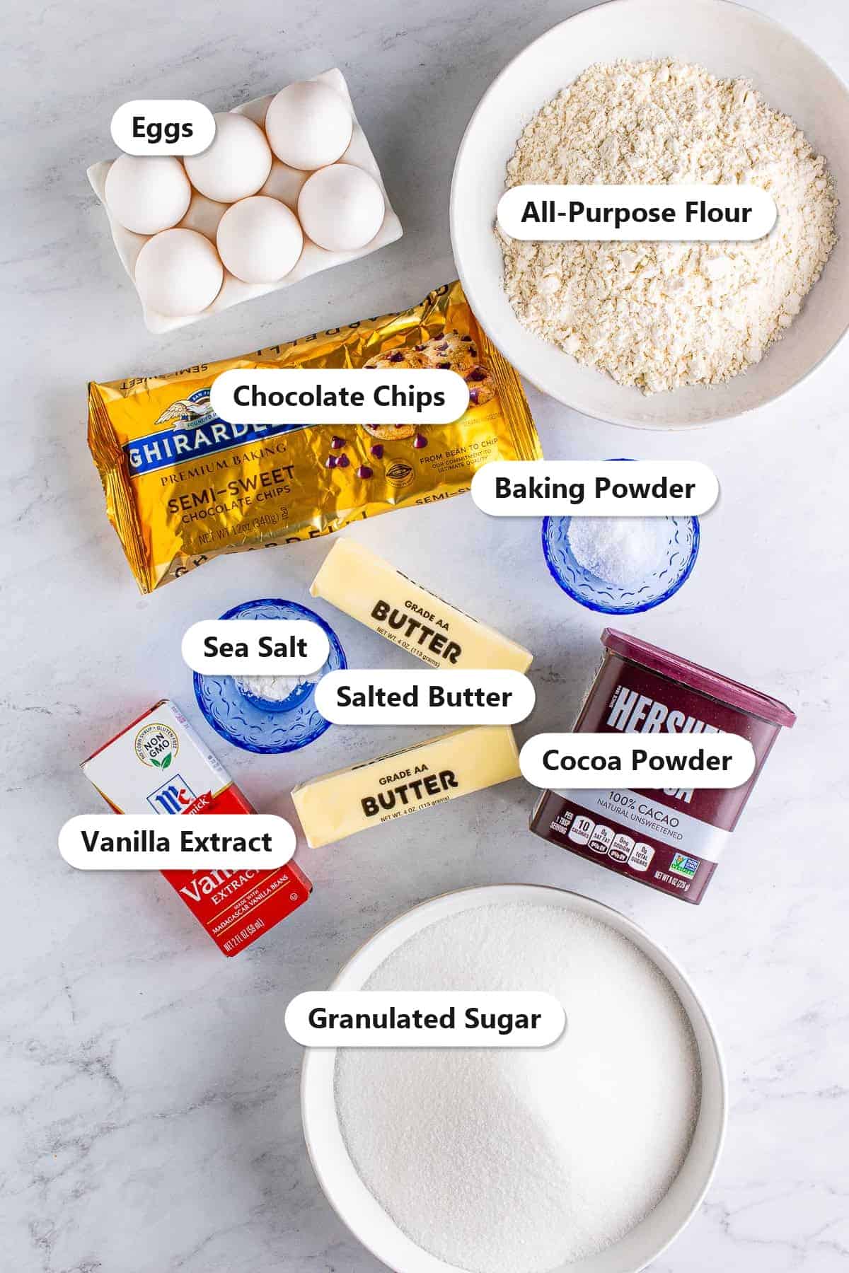 Labeled ingredients to make fudgy brownies: eggs, all-purpose flour, chocolate chips, baking powder, salted butter, cocoa powder, sea salt, vanilla extract, and granulated sugar.