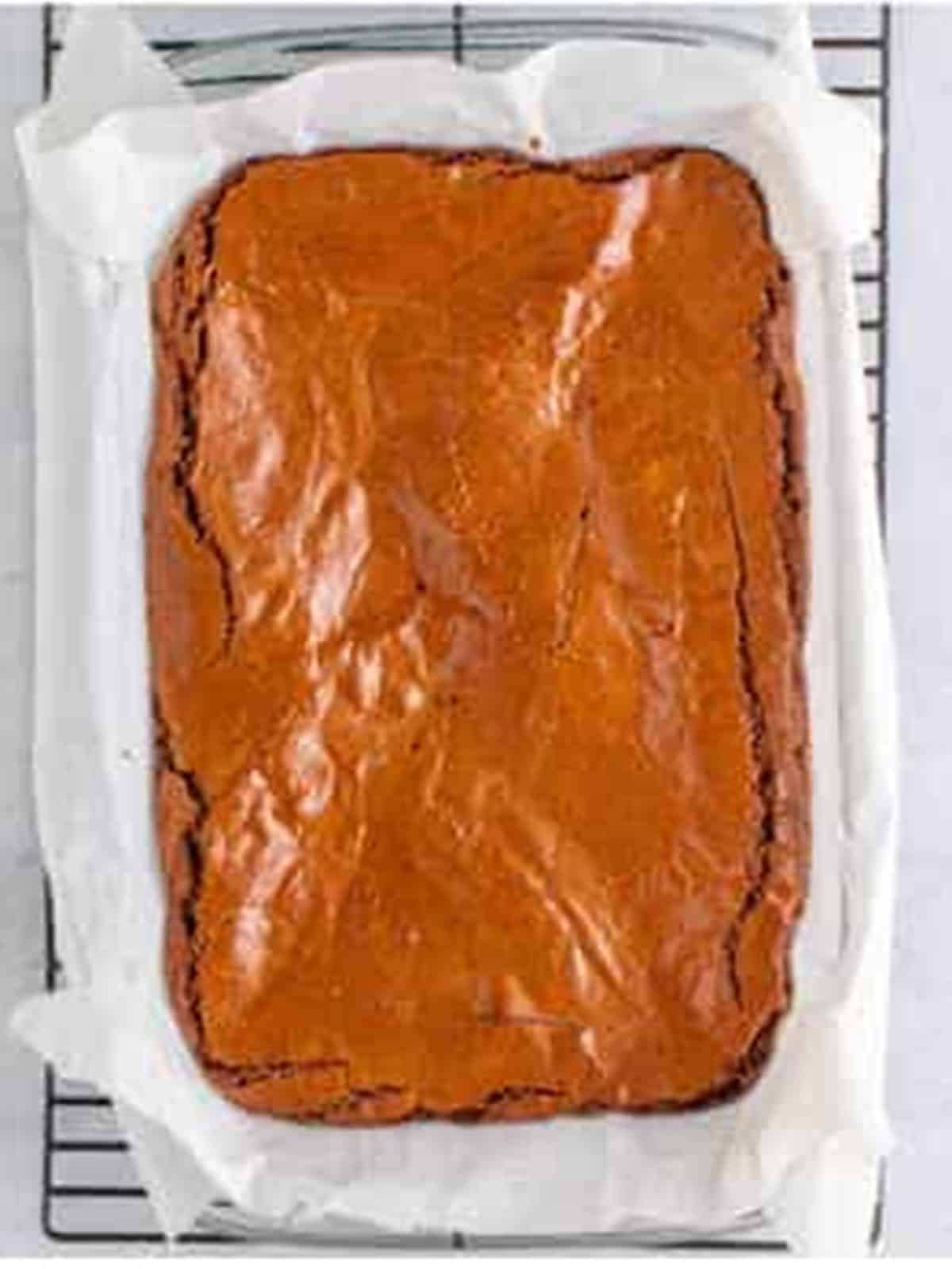 Baked fudgy brownies in a parchment-lined pan cooling on a wire rack.