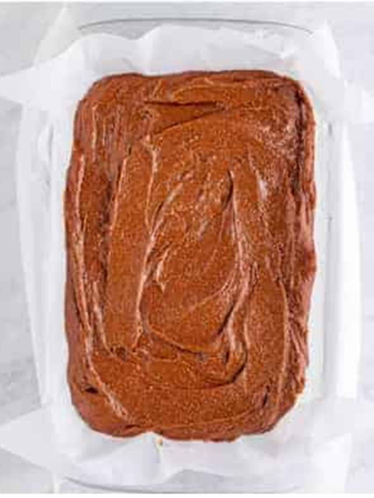 Brownie batter spread evenly into a parchment-lined baking pan.