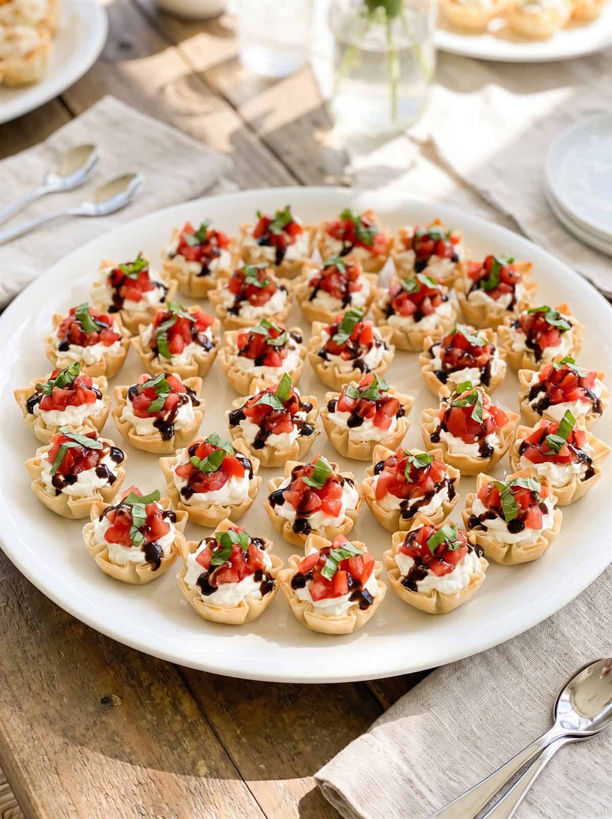 A platter of creamy bruschetta bites in mini phyllo cups topped with tomato basil bruschetta.