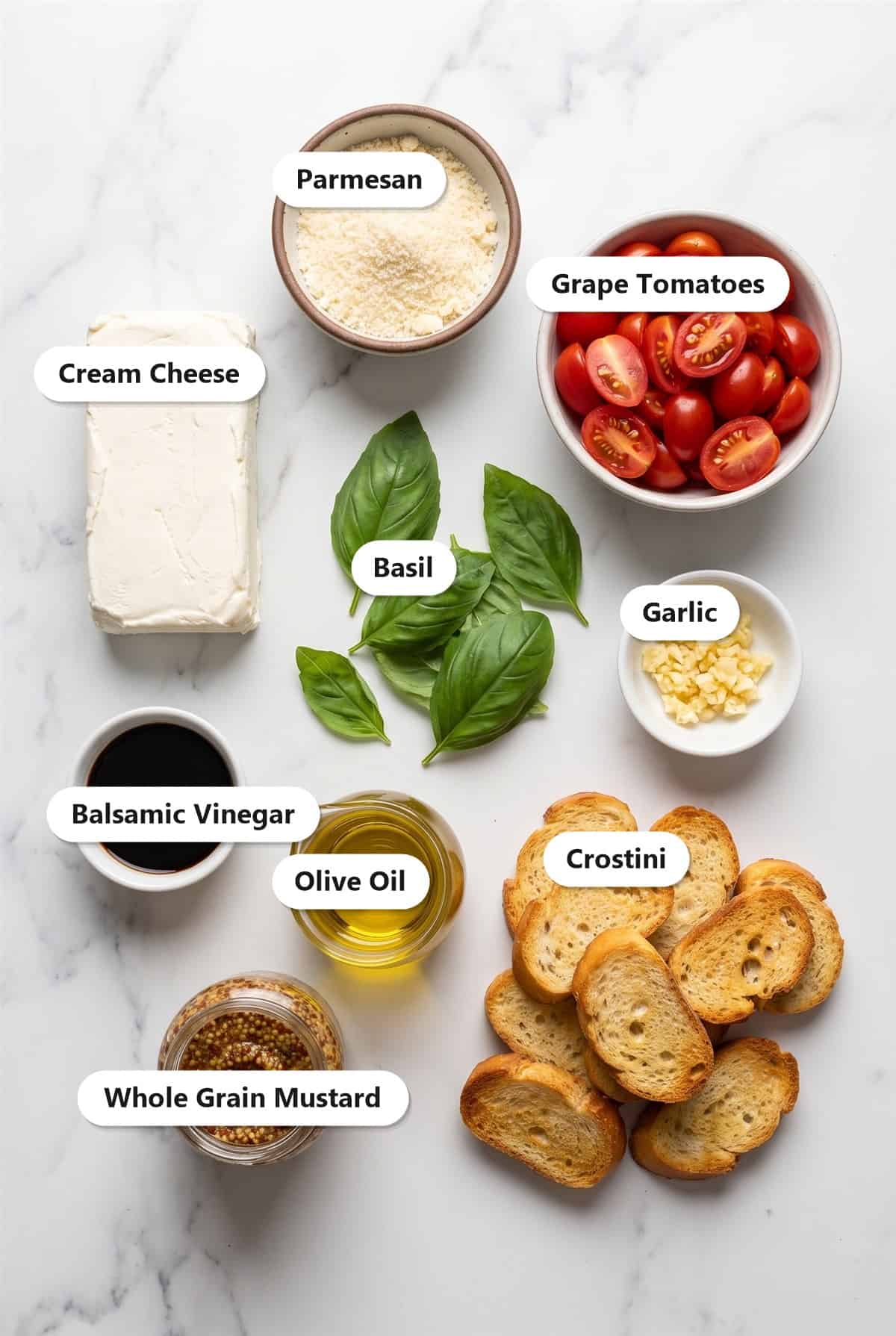 Ingredients to make creamy bruschetta dip including cream cheese, parmesan, grape tomatoes, basil, garlic, balsamic vinegar, olive oil, mustard, and crostini.