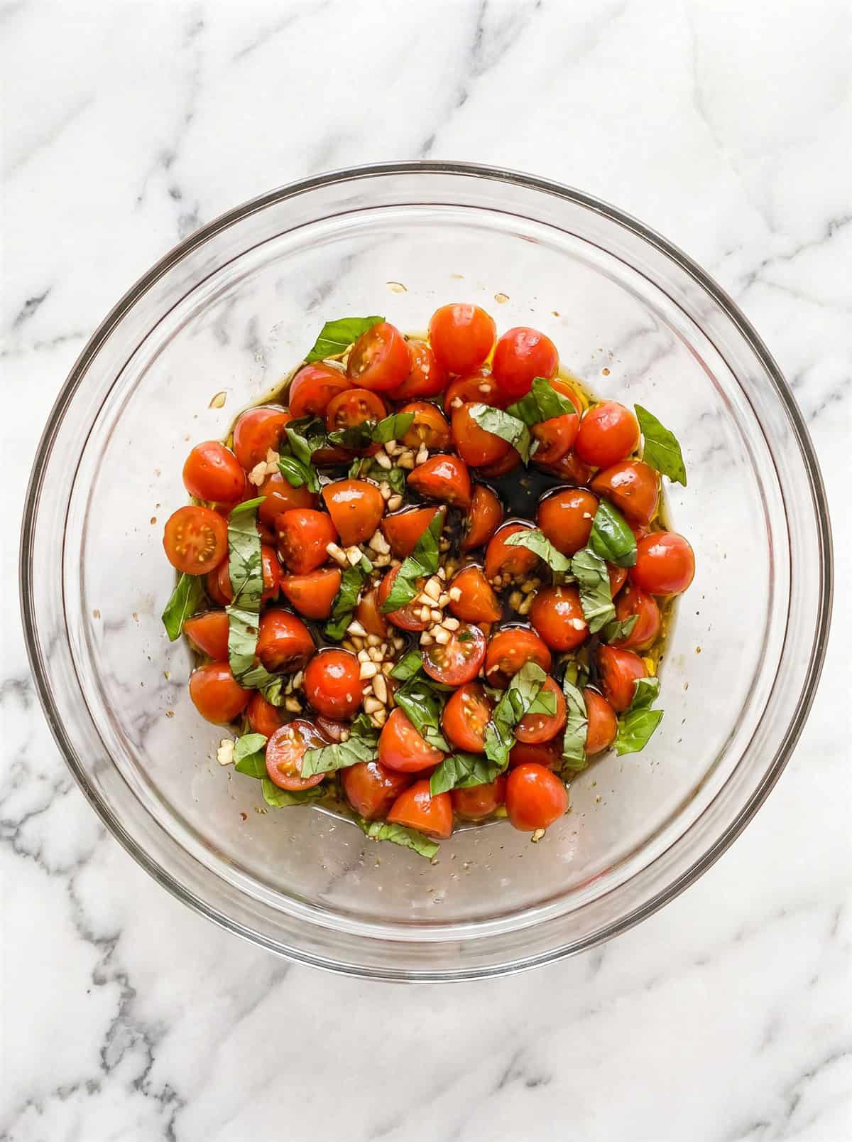 Diced tomatoes, basil, garlic, balsamic, and olive oil tossed together for bruschetta topping in a glass bowl.