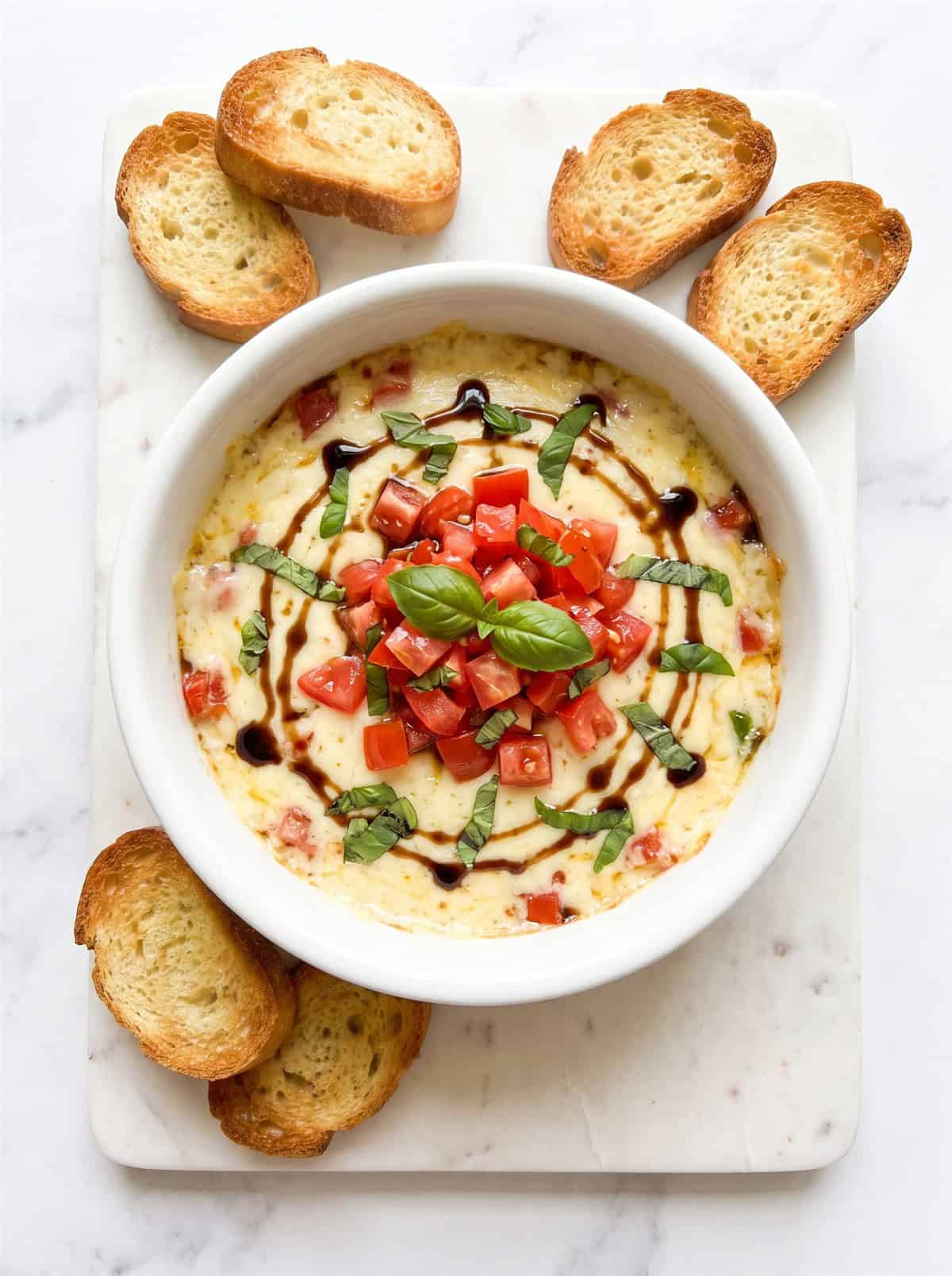 Finished creamy bruschetta dip topped with marinated tomatoes and basil, served with crostini.