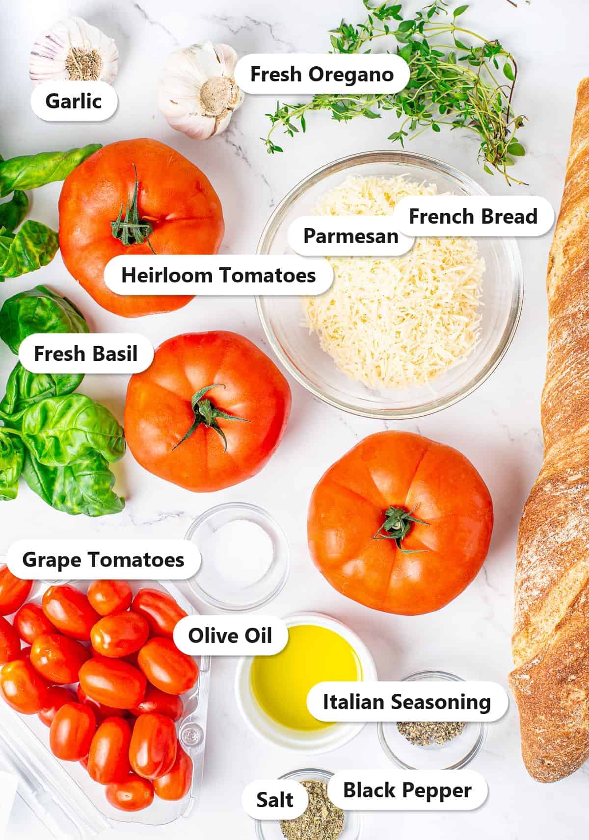 Labeled ingredients for bruschetta including heirloom tomatoes, grape tomatoes, fresh basil, garlic, parmesan, olive oil, and a French bread loaf.