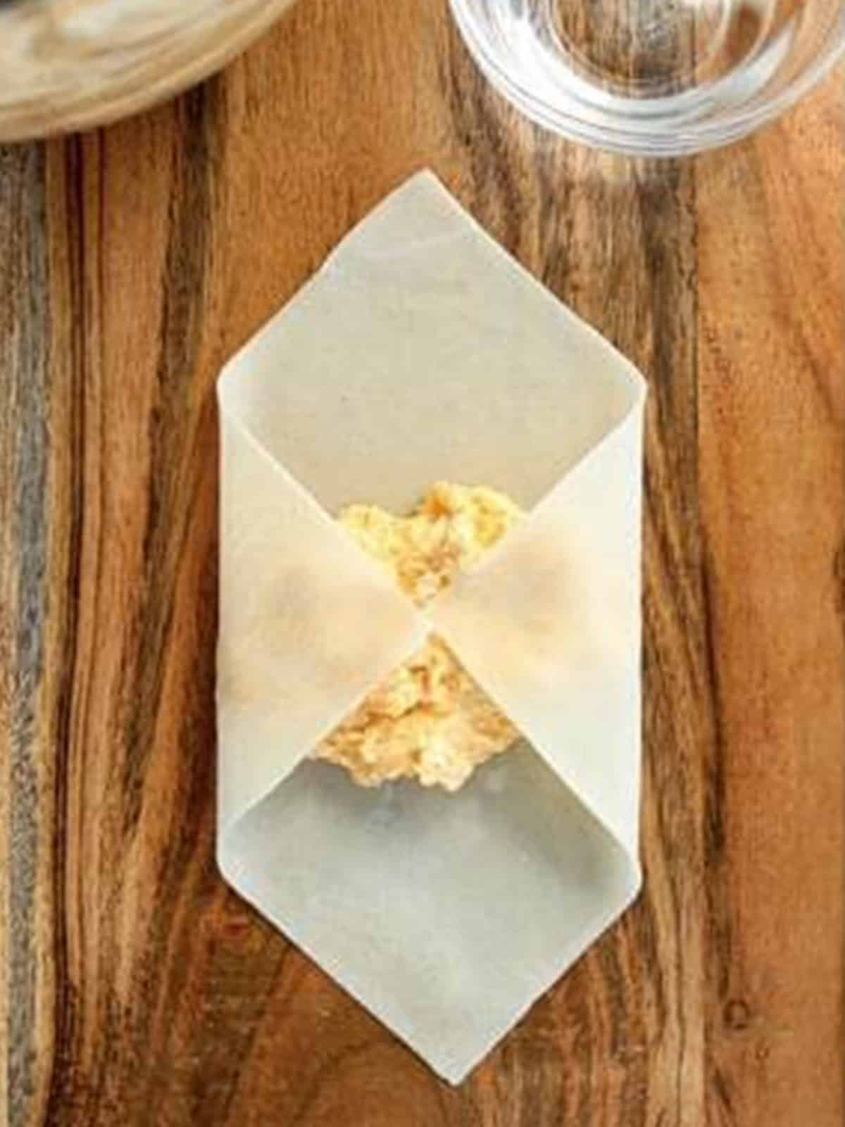 Folding the sides of an egg roll wrapper over the buffalo chicken filling.
