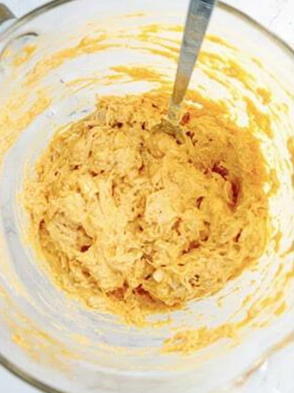 Canned chicken, cream cheese, and buffalo sauce mixed in a bowl for buffalo chicken egg rolls.