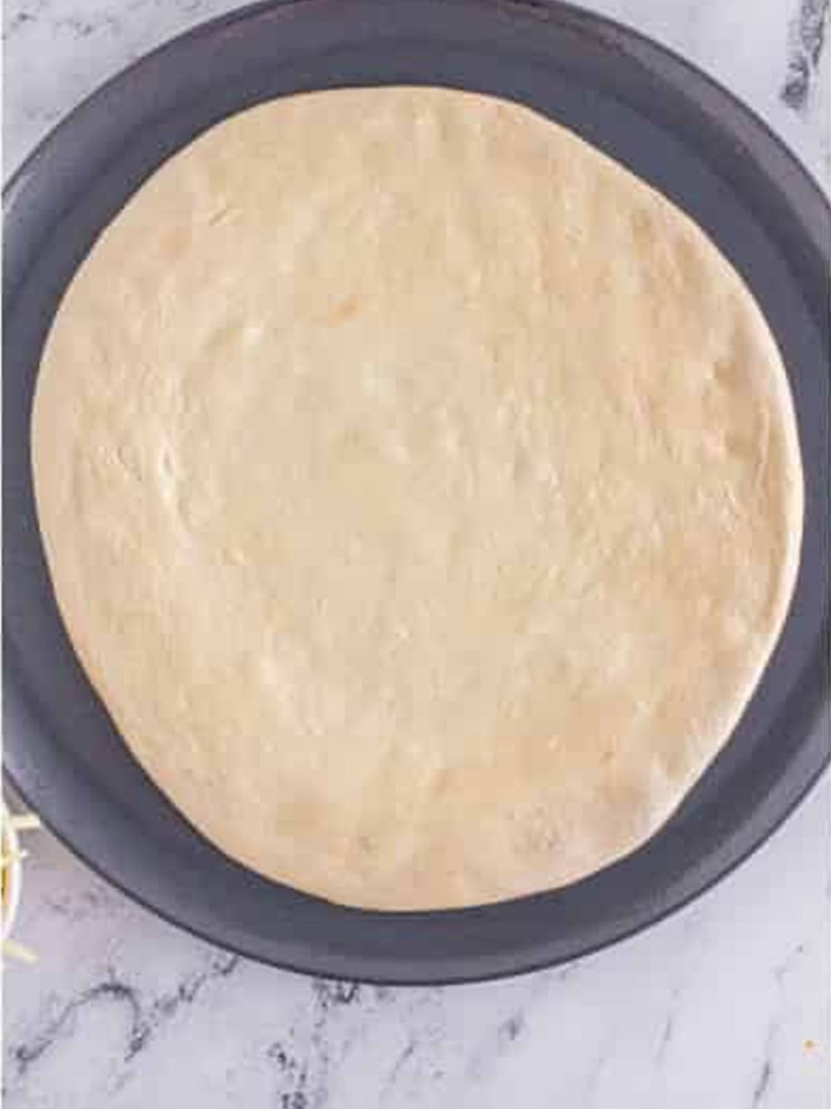 Pizza dough spread out on a greased pizza pan.