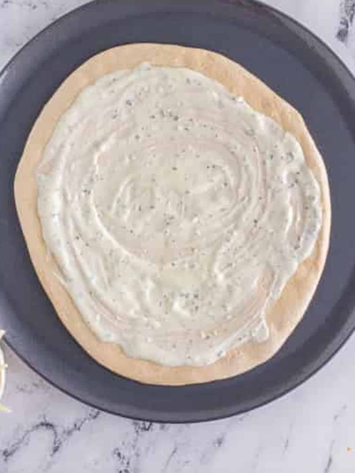 Ranch dressing spread over the pizza dough leaving a border.