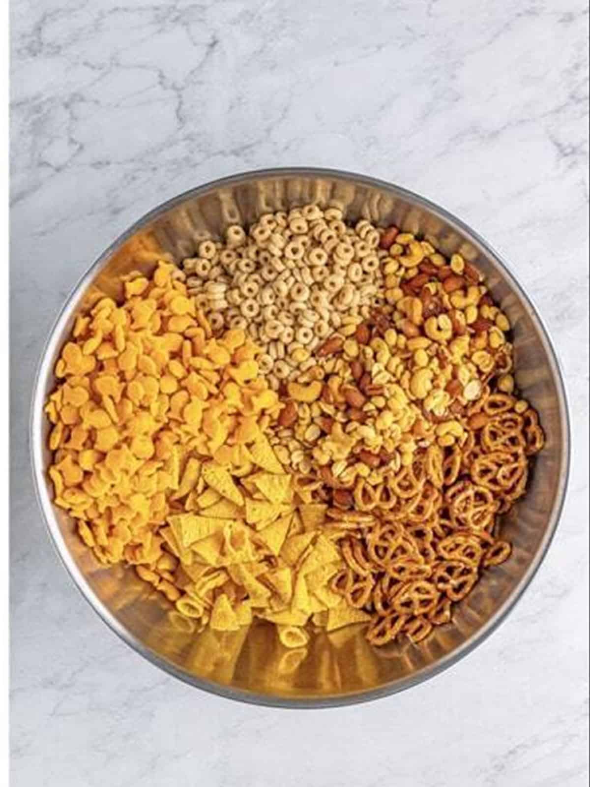 Bugles, mixed nuts, pretzels, Cheerios, and Goldfish added to a large bowl.