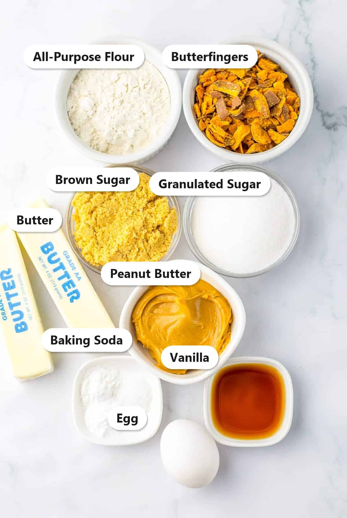 Labeled ingredients for butterfinger cookies including flour, chopped Butterfingers, peanut butter, butter, sugars, and egg.