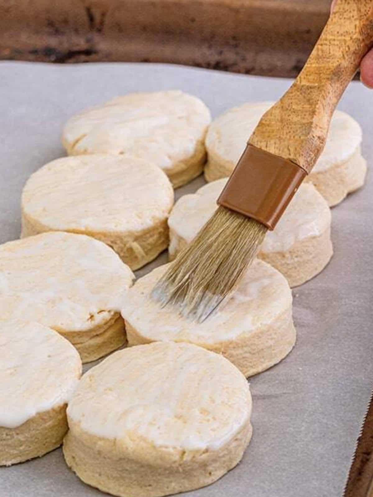 Brushing the tops of buttermilk biscuits with buttermilk before baking.