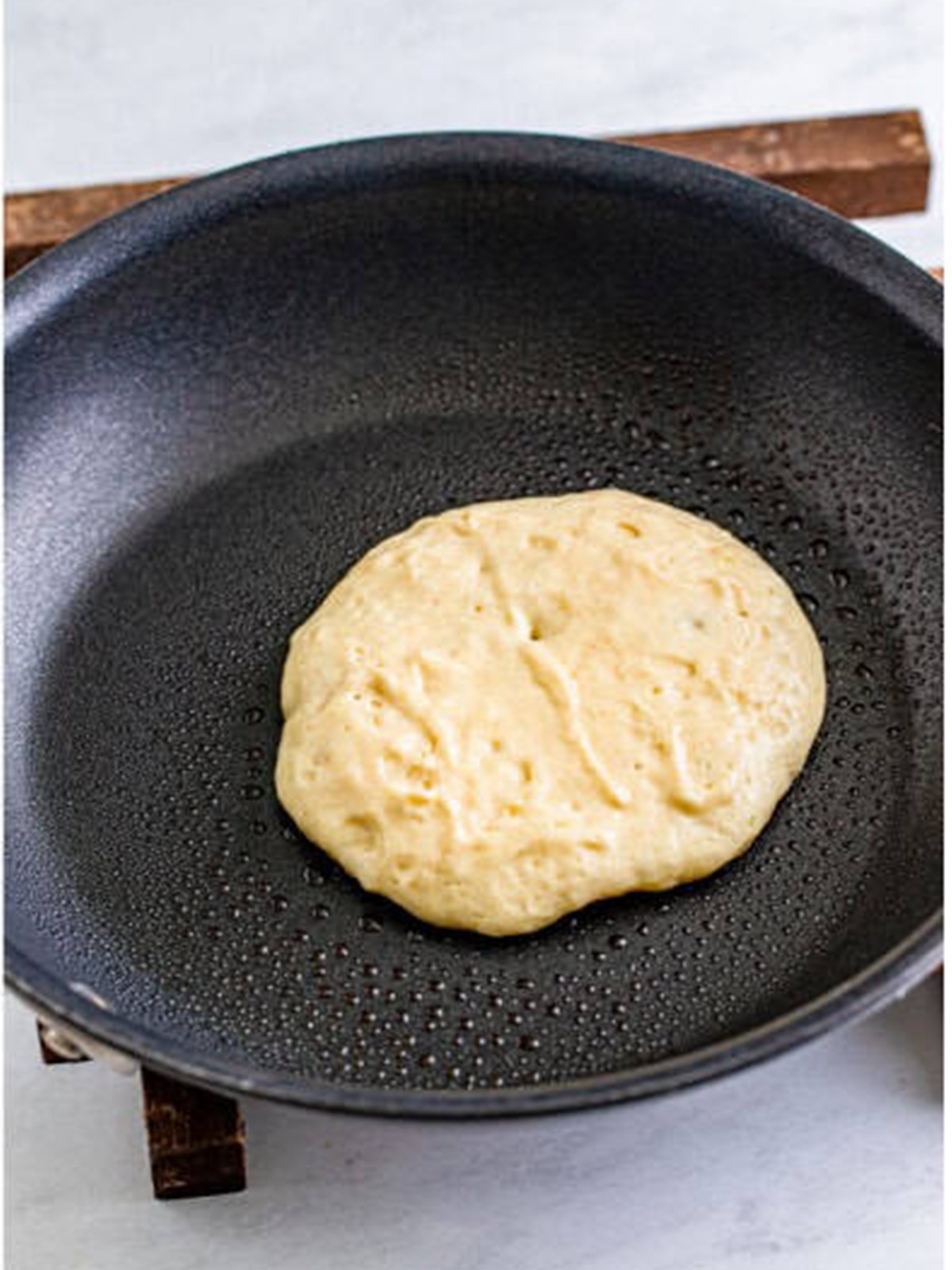 A Buttermilk Pancake cooking in a nonstick skillet until bubbles form.