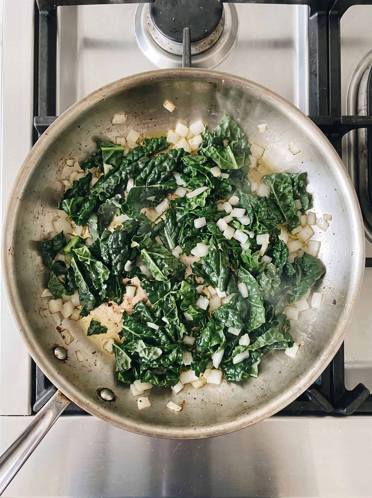 Chopped kale and onion sauteing in a skillet.