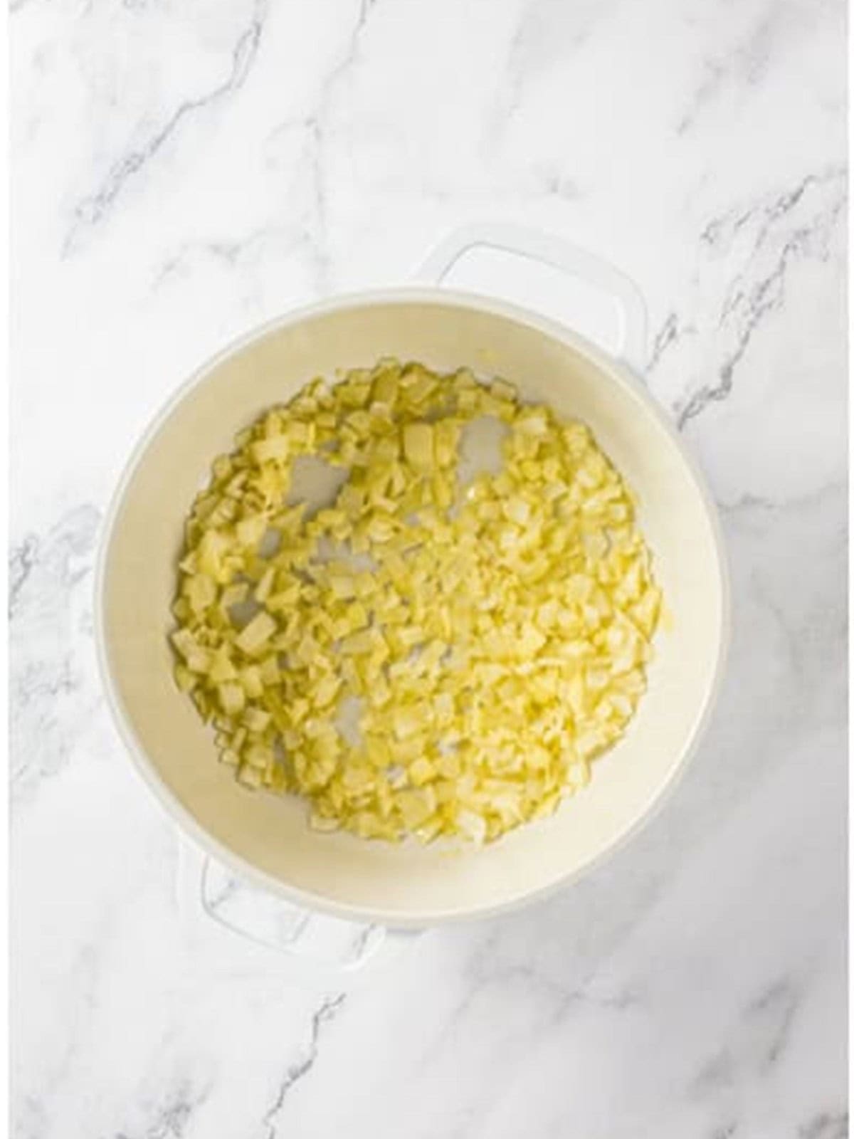 Sauteing diced onion and garlic in butter in a white pot.