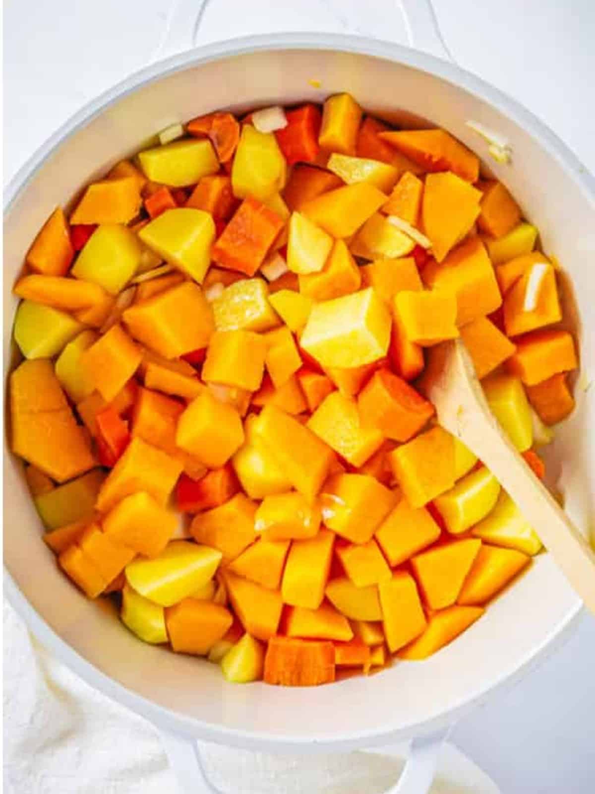 Diced butternut squash, potato, carrot, and onion in a white pot to start butternut squash soup.