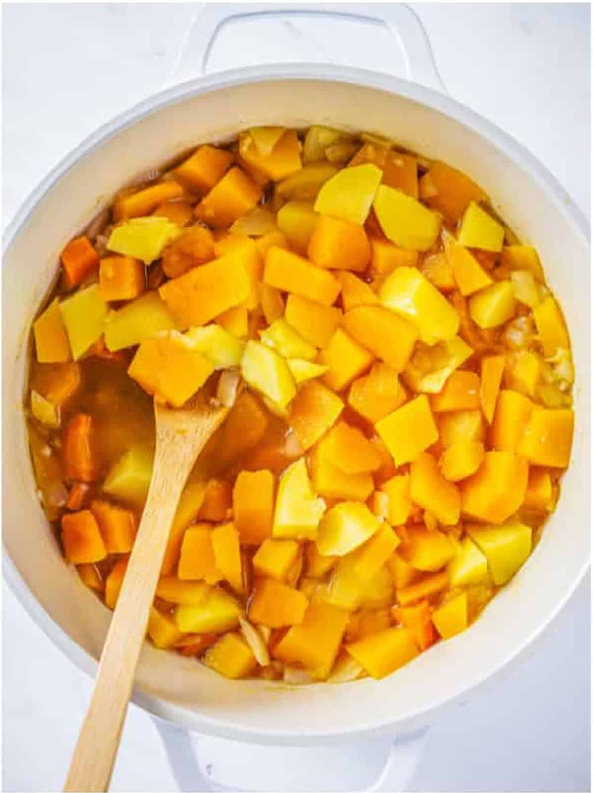 Vegetables simmering in broth in a white pot for butternut squash soup.
