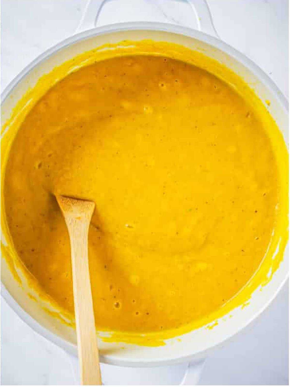 Smooth and creamy blended butternut squash soup in a pot with a wooden spoon.