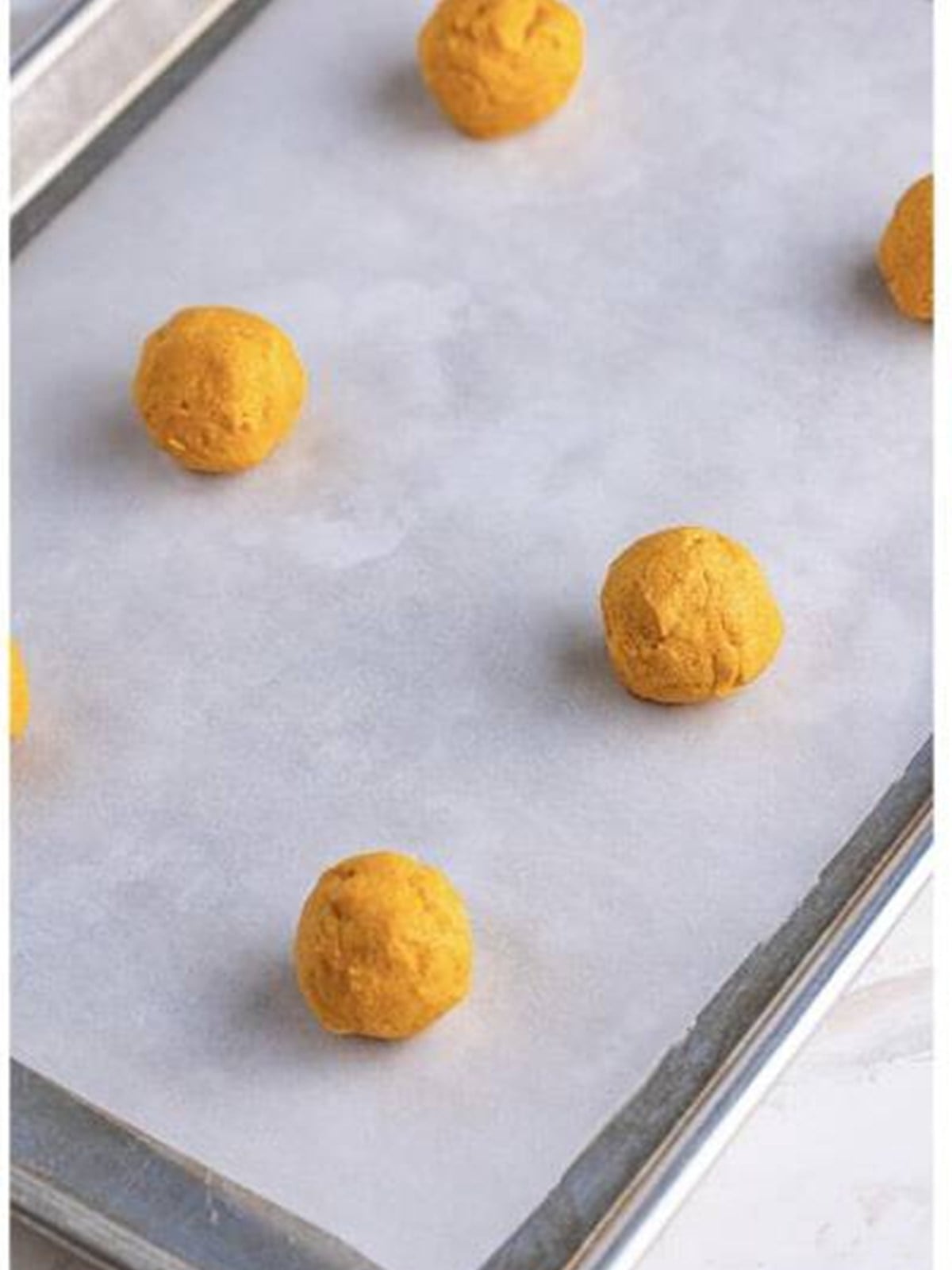 Scooped balls of butterscotch cookie dough on a parchment-lined baking sheet.