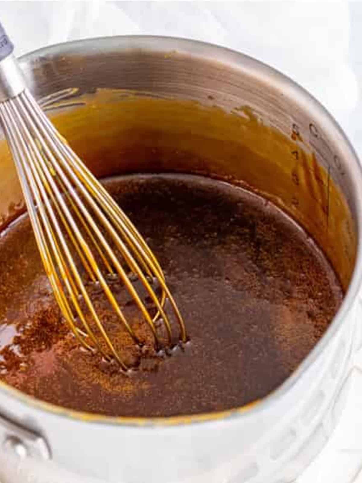 Butterscotch sauce boiling and being whisked smooth in a saucepan.