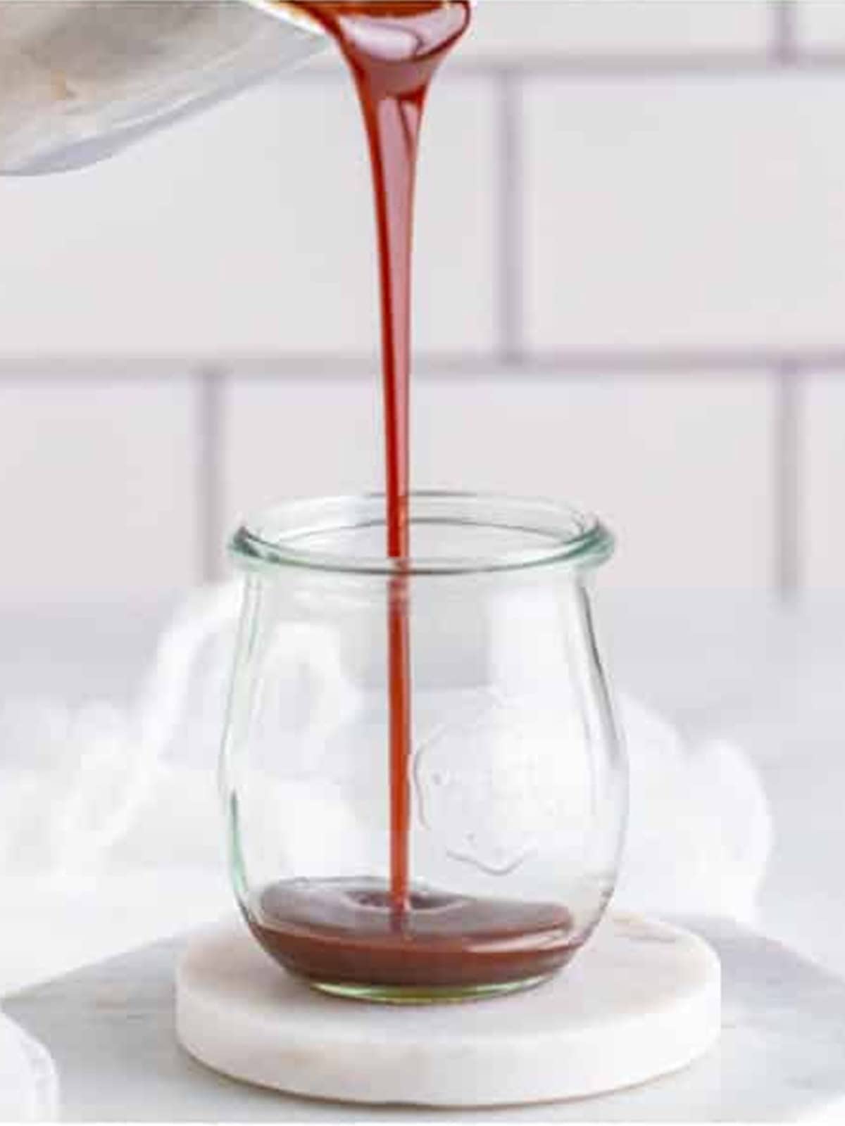 Finished butterscotch sauce being poured into a glass jar.