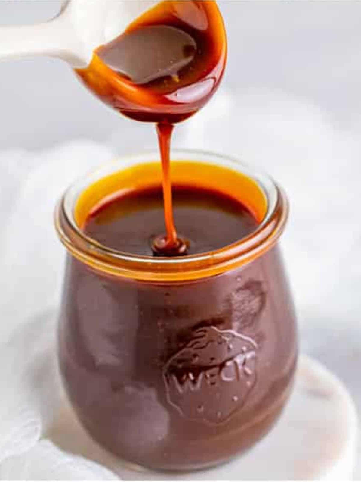 A jar of glossy homemade butterscotch sauce with a drip down the side.