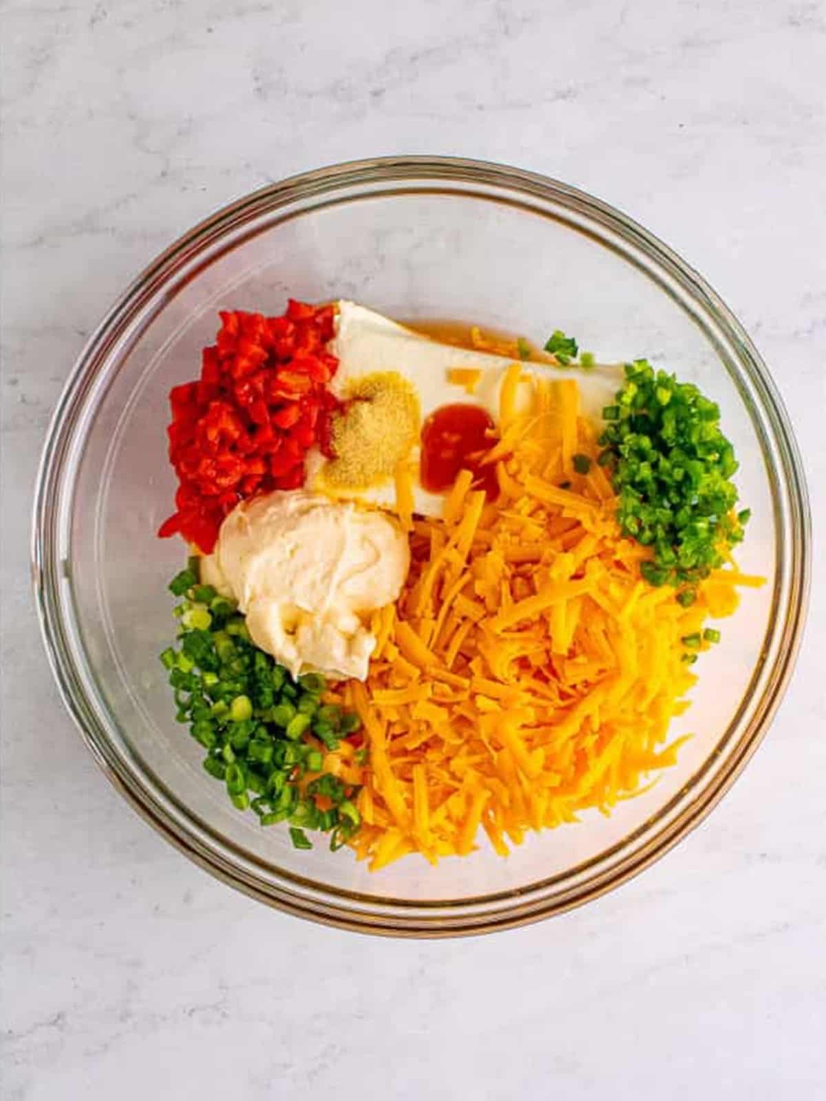 Cheddar, cream cheese, mayonnaise, pimentos, and seasonings in a bowl before mixing.