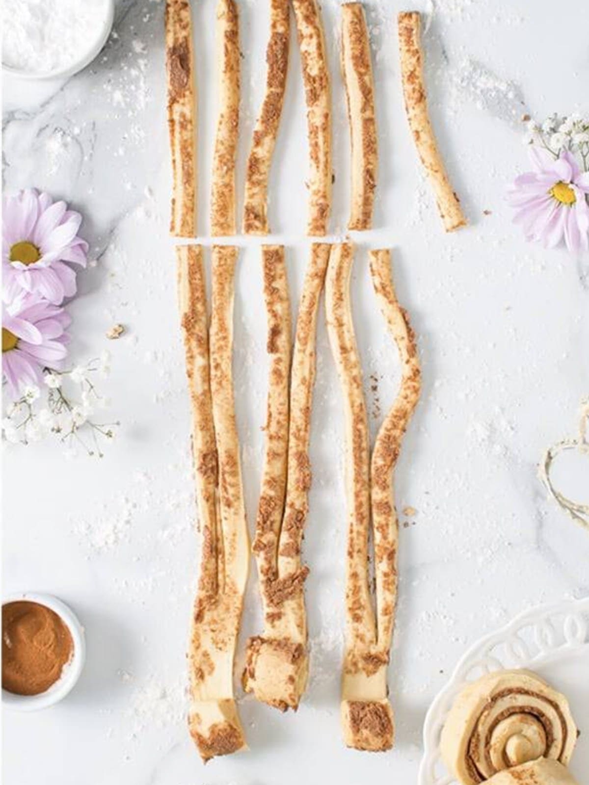 Unraveled canned cinnamon roll dough cut into strips on a marble surface.