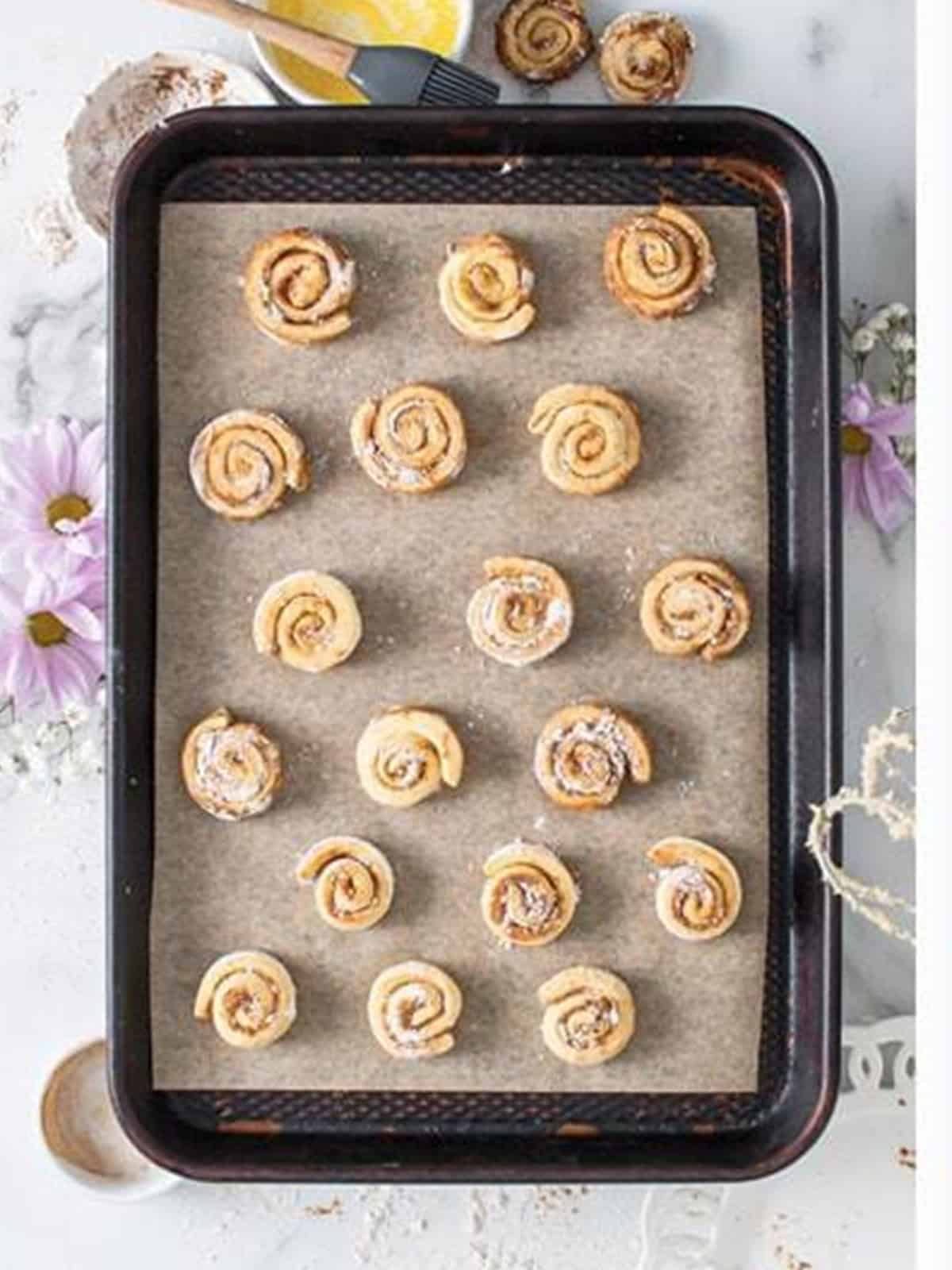 Mini cinnamon rolls arranged on a parchment lined baking sheet.