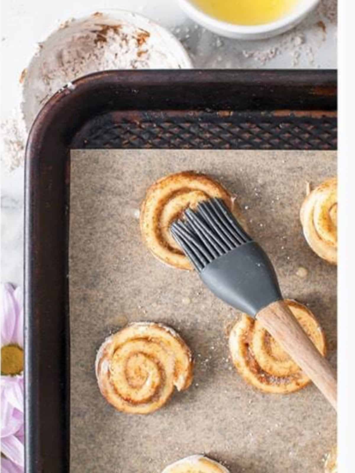 Brushing melted butter over the mini cinnamon rolls before baking.