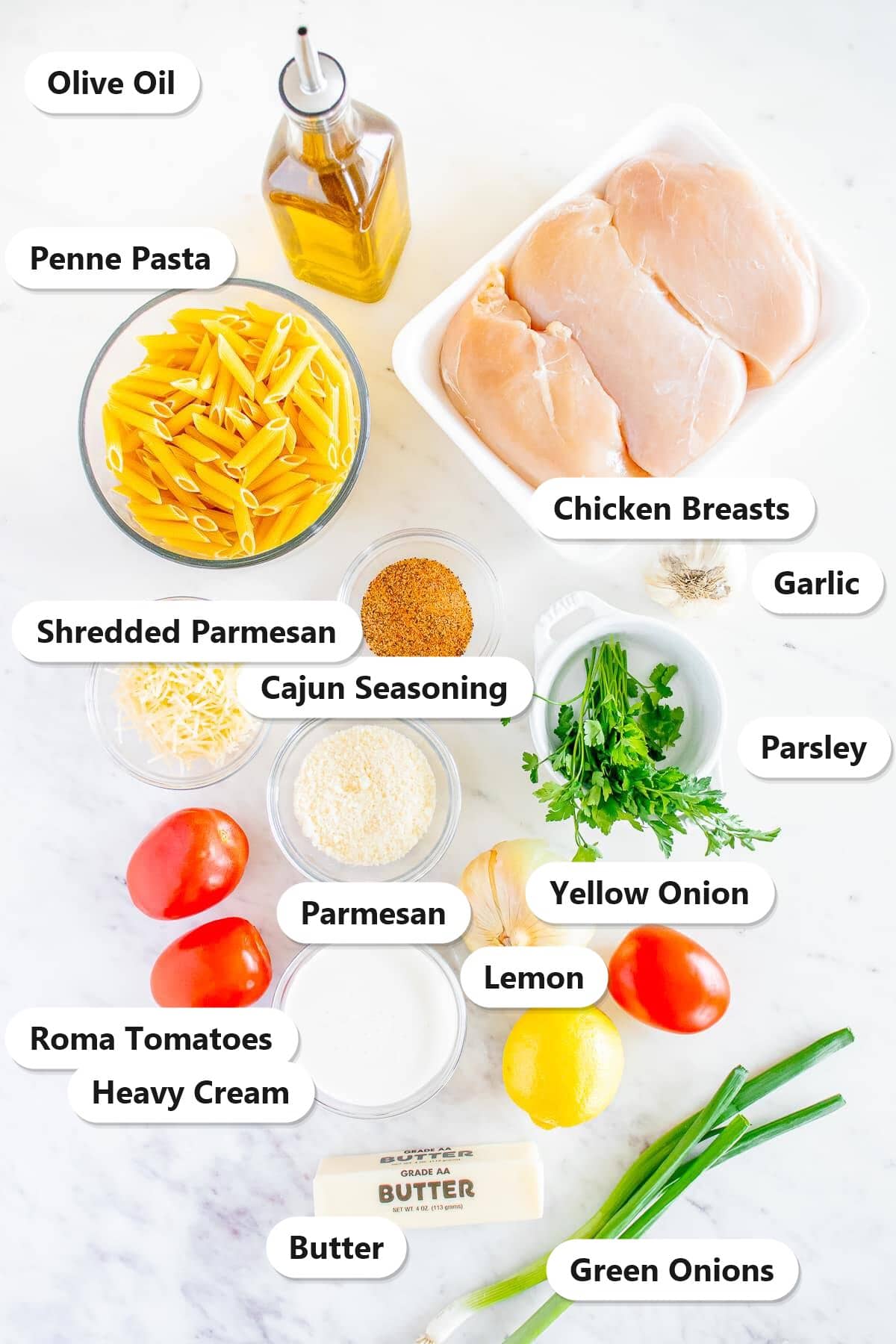 Ingredients to make Cajun Chicken Pasta laid out and labeled on a marble counter.