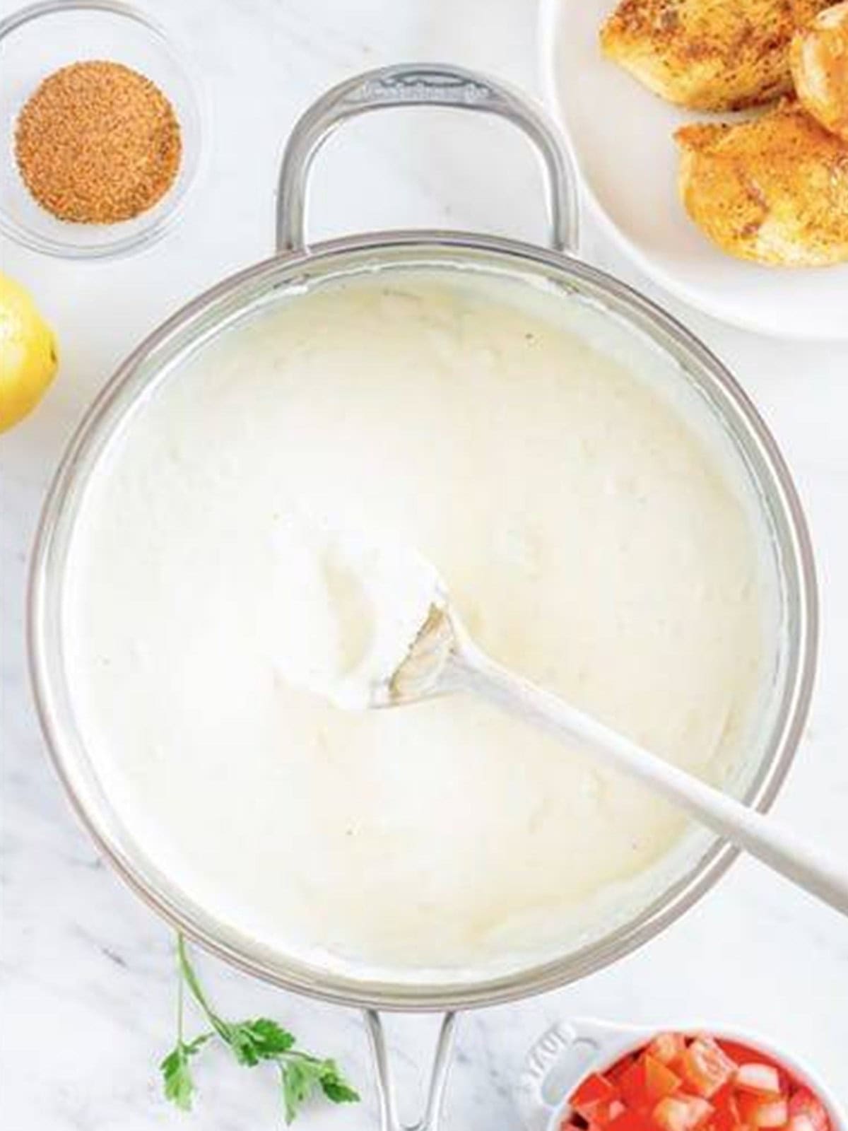 Thickened cream sauce for Cajun Chicken Pasta in a skillet with a wooden spoon.