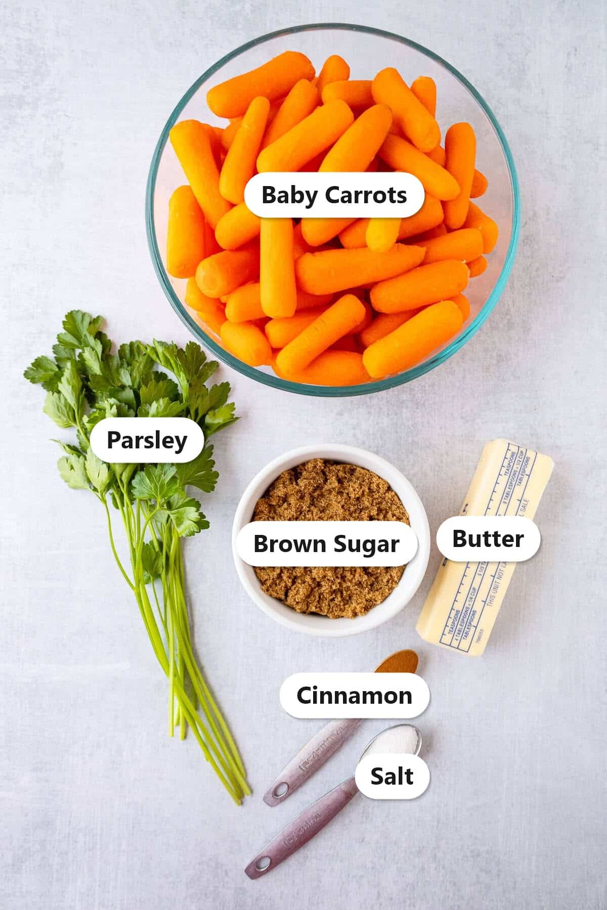 Labeled ingredients for brown sugar cinnamon candied carrots including baby carrots, brown sugar, butter, cinnamon, salt, and parsley.