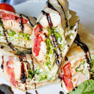 Stacked caprese chicken wraps cut in half showing chicken, tomato, basil, and balsamic glaze.