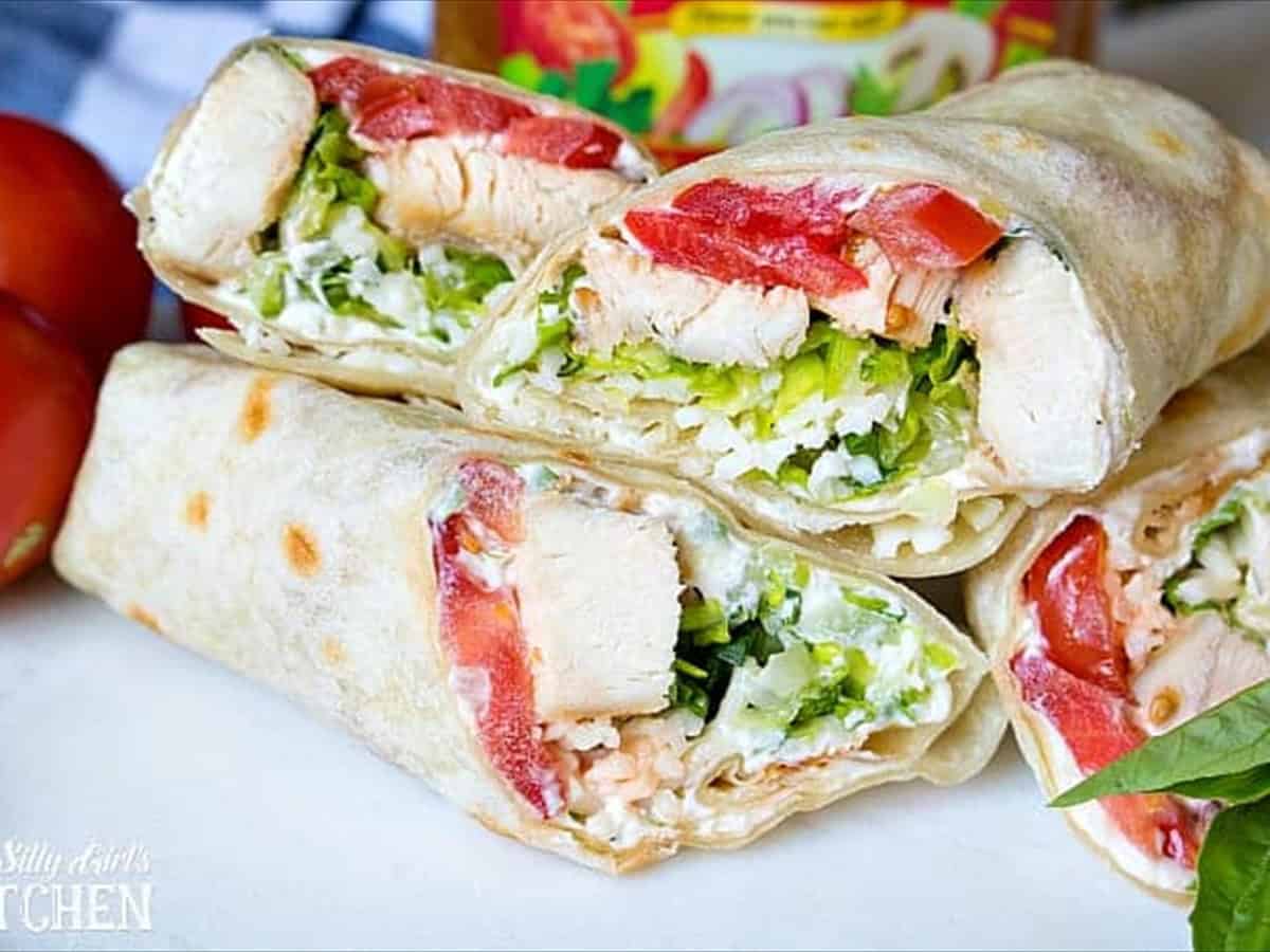 Caprese chicken wraps stacked on a board with cherry tomatoes and fresh basil.