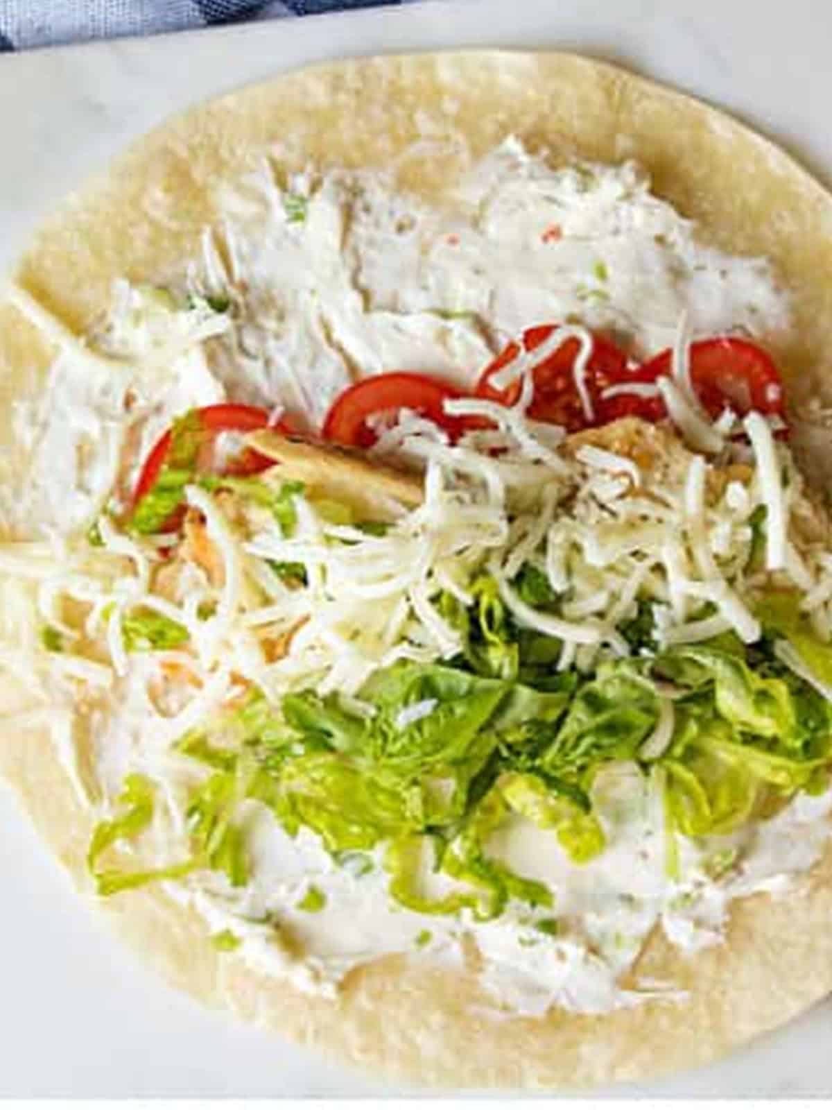 Shredded mozzarella added on top of the lettuce and basil in a caprese chicken wrap.