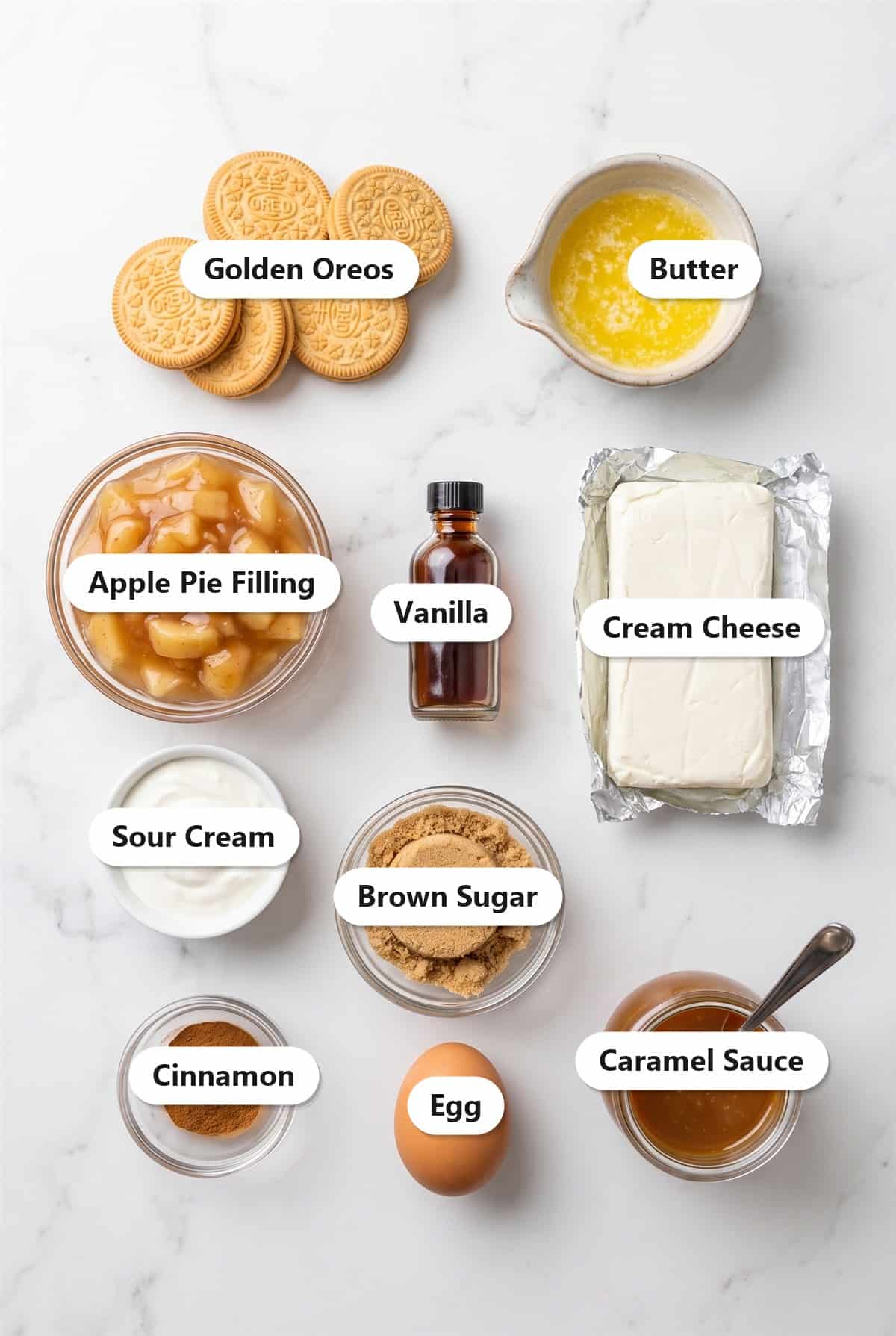 Labeled ingredients for caramel apple cheesecake bars including golden Oreos, butter, apple pie filling, cream cheese, sour cream, brown sugar, vanilla, cinnamon, egg, and caramel sauce.
