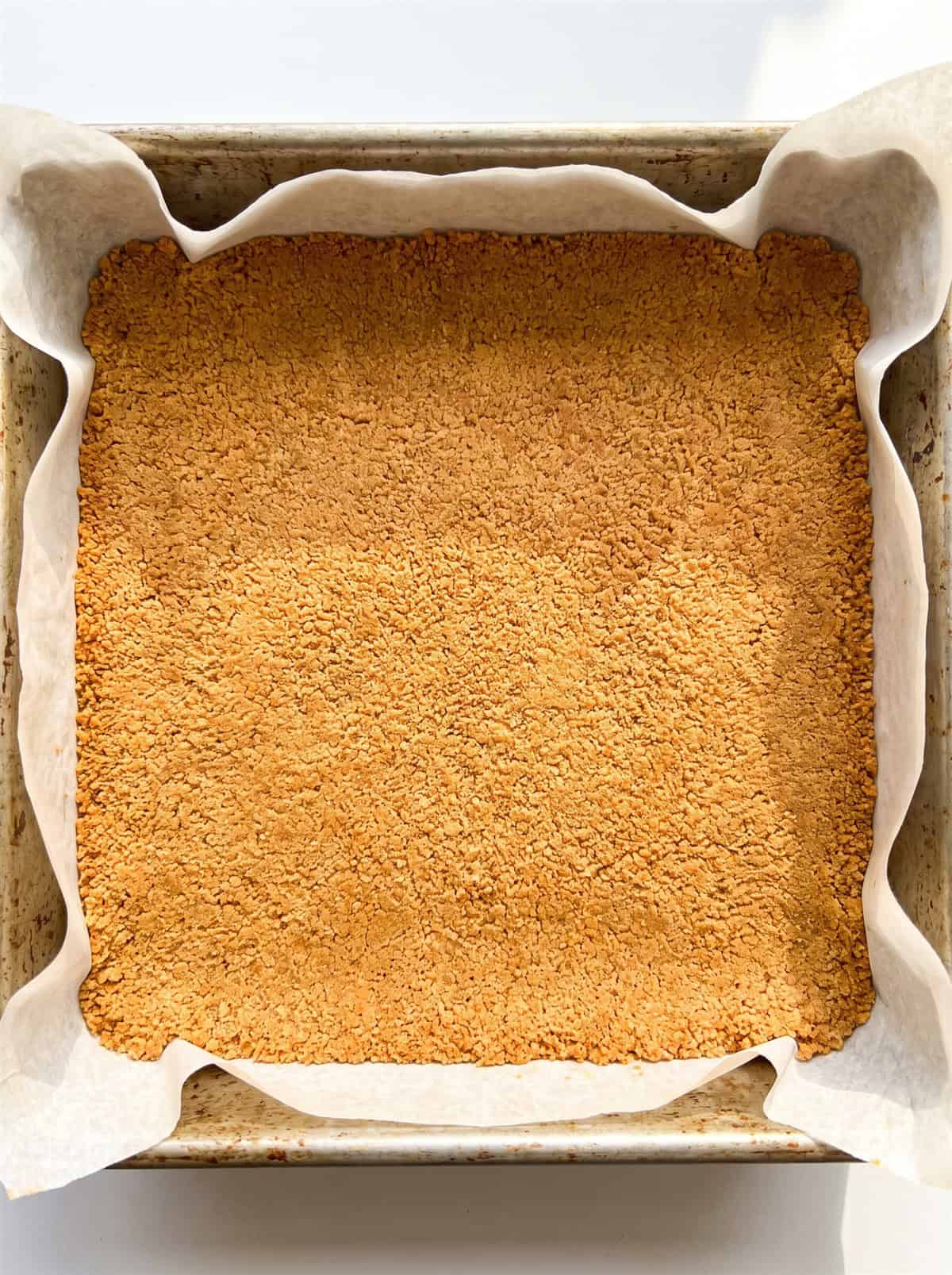 Golden cookie crumb crust pressed into a parchment-lined baking pan.