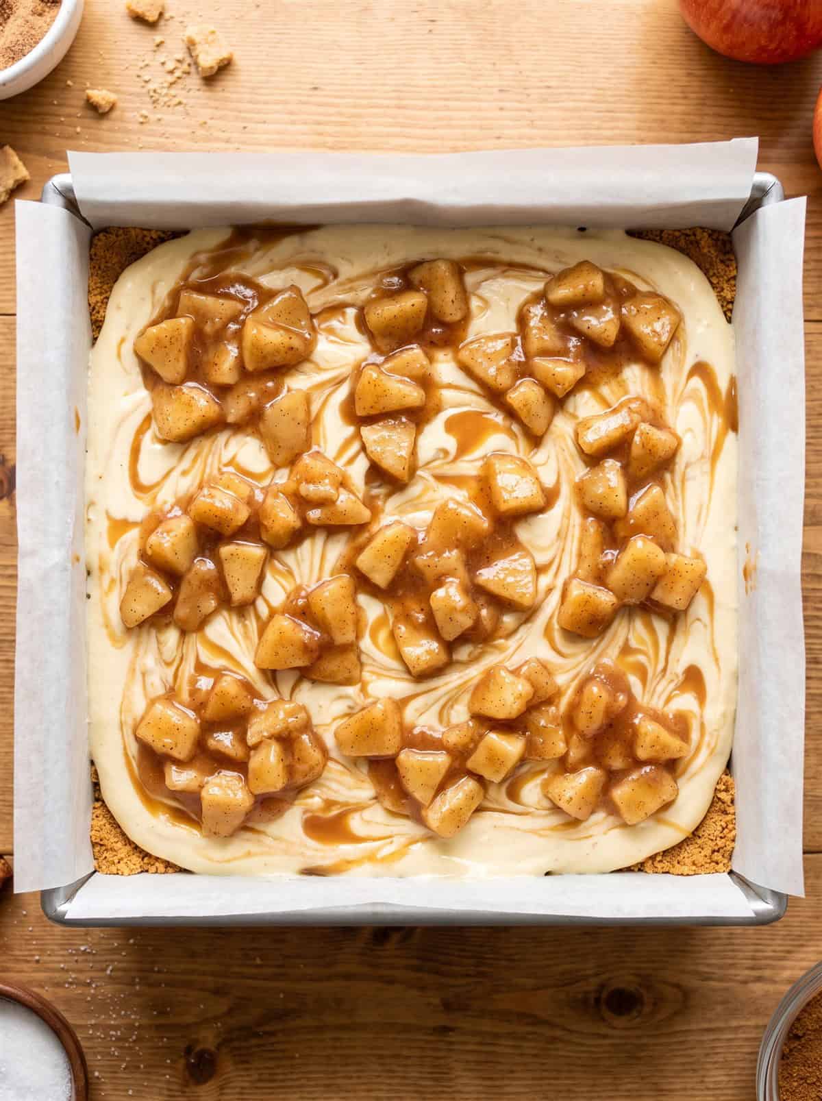 Unbaked caramel apple cheesecake topped with chopped spiced apples in a pan.