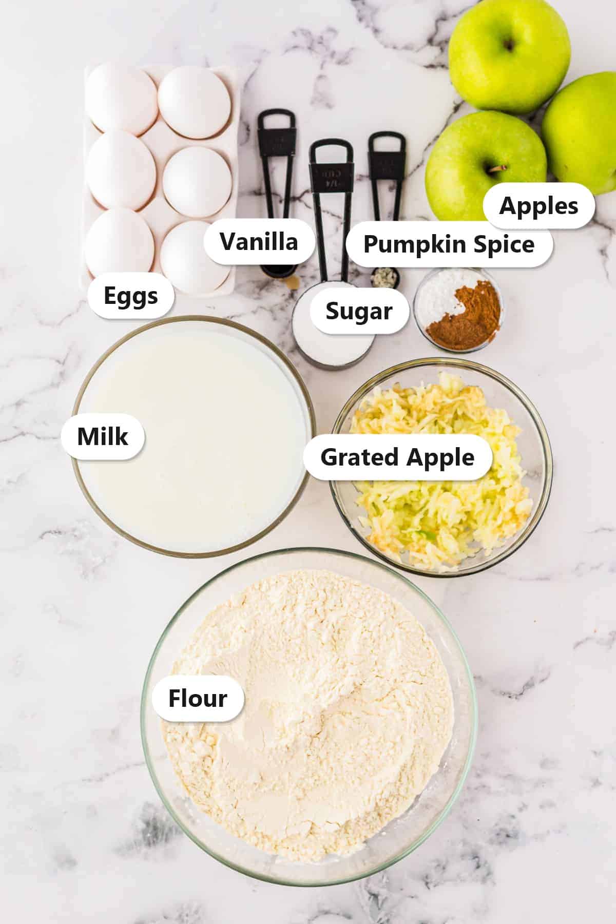 Labeled ingredients for caramel apple funnel cakes including eggs, vanilla, sugar, pumpkin spice, Granny Smith apples, milk, grated apple, and flour.