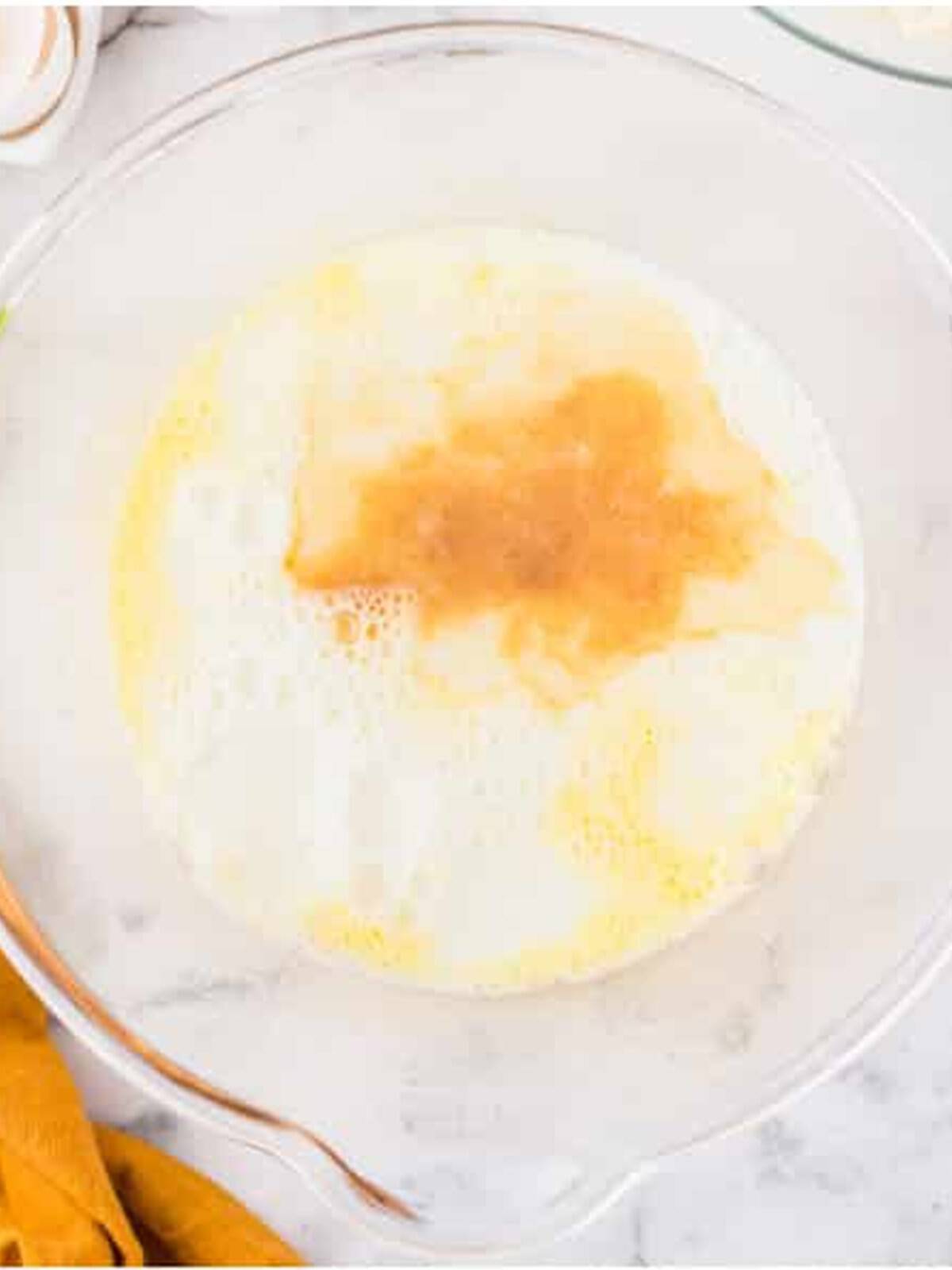 Eggs, sugar, milk, and vanilla whisked together in a glass bowl for funnel cake batter.