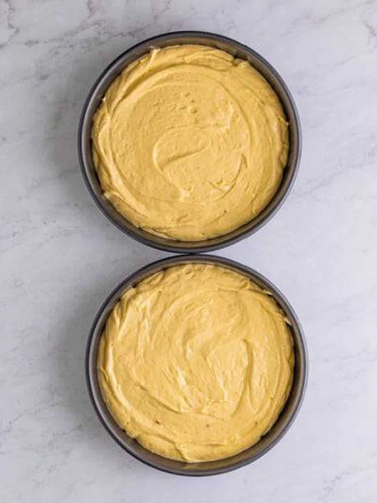 Caramel cake batter divided evenly between two round cake pans.