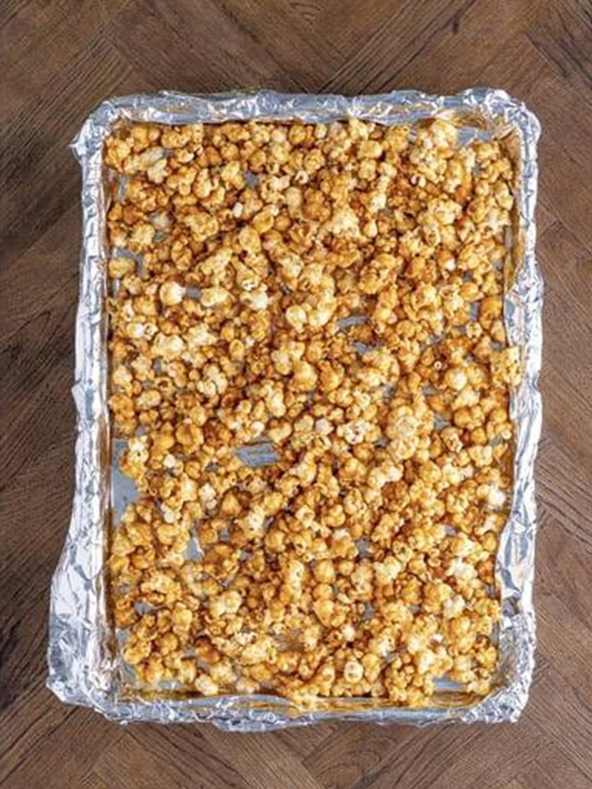 Baked caramel corn spread out on parchment to cool and break apart.