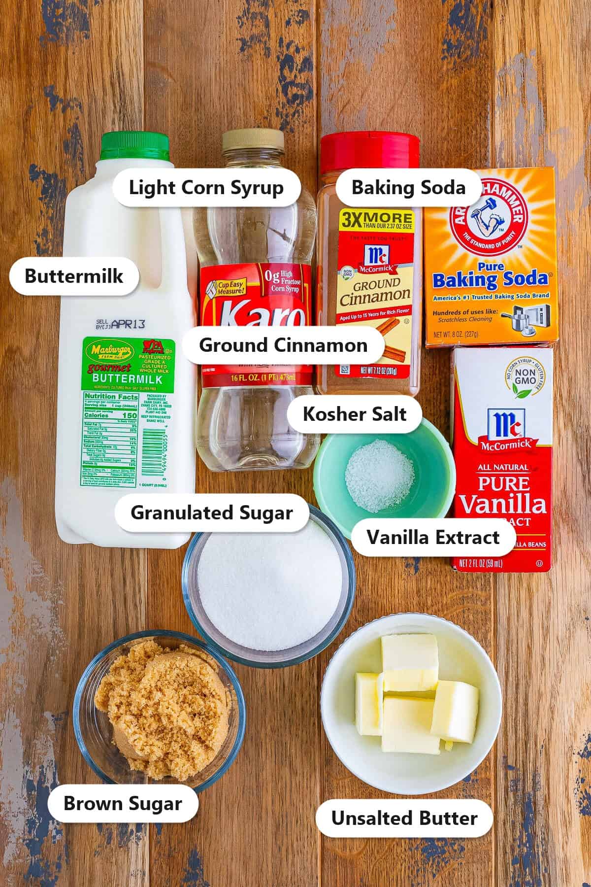 Labeled ingredients for caramel sauce including buttermilk, granulated sugar, brown sugar, butter, cinnamon, and vanilla on a wood board.