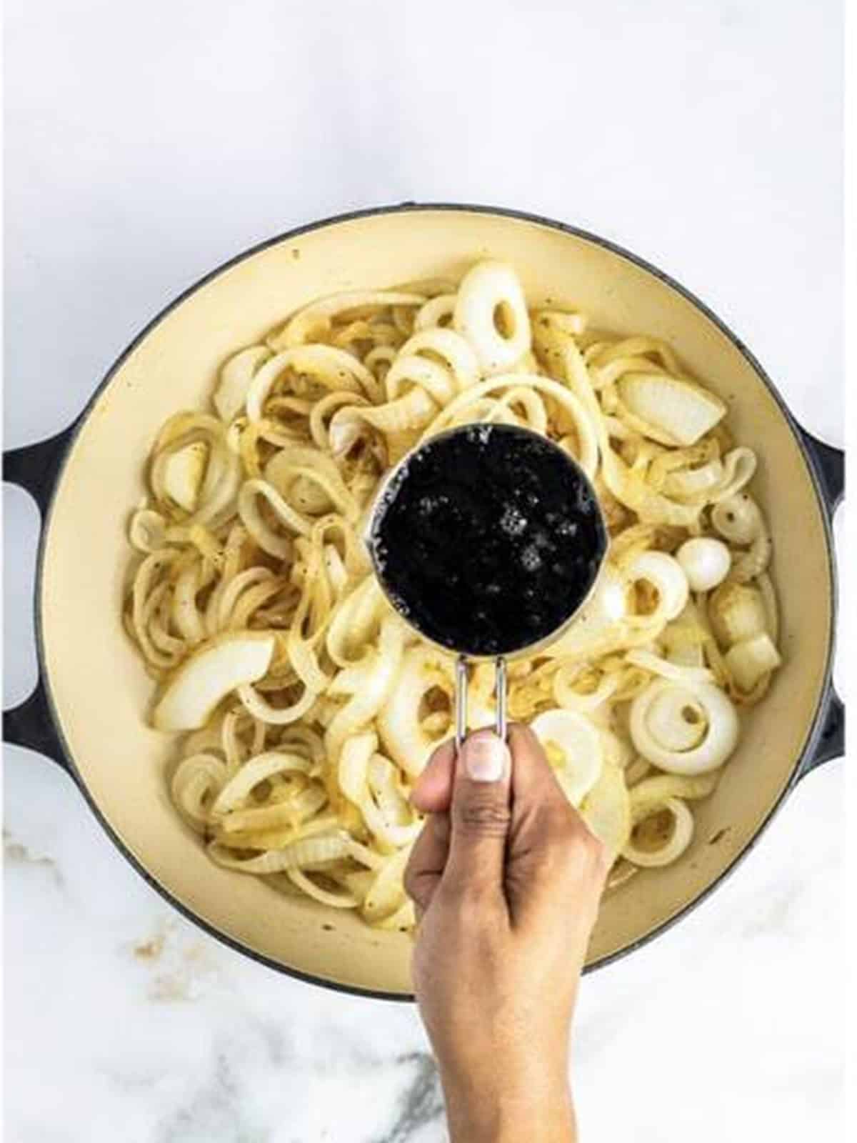 Pouring Coca-Cola into a skillet of softened sweet onions for Caramelized Onions.